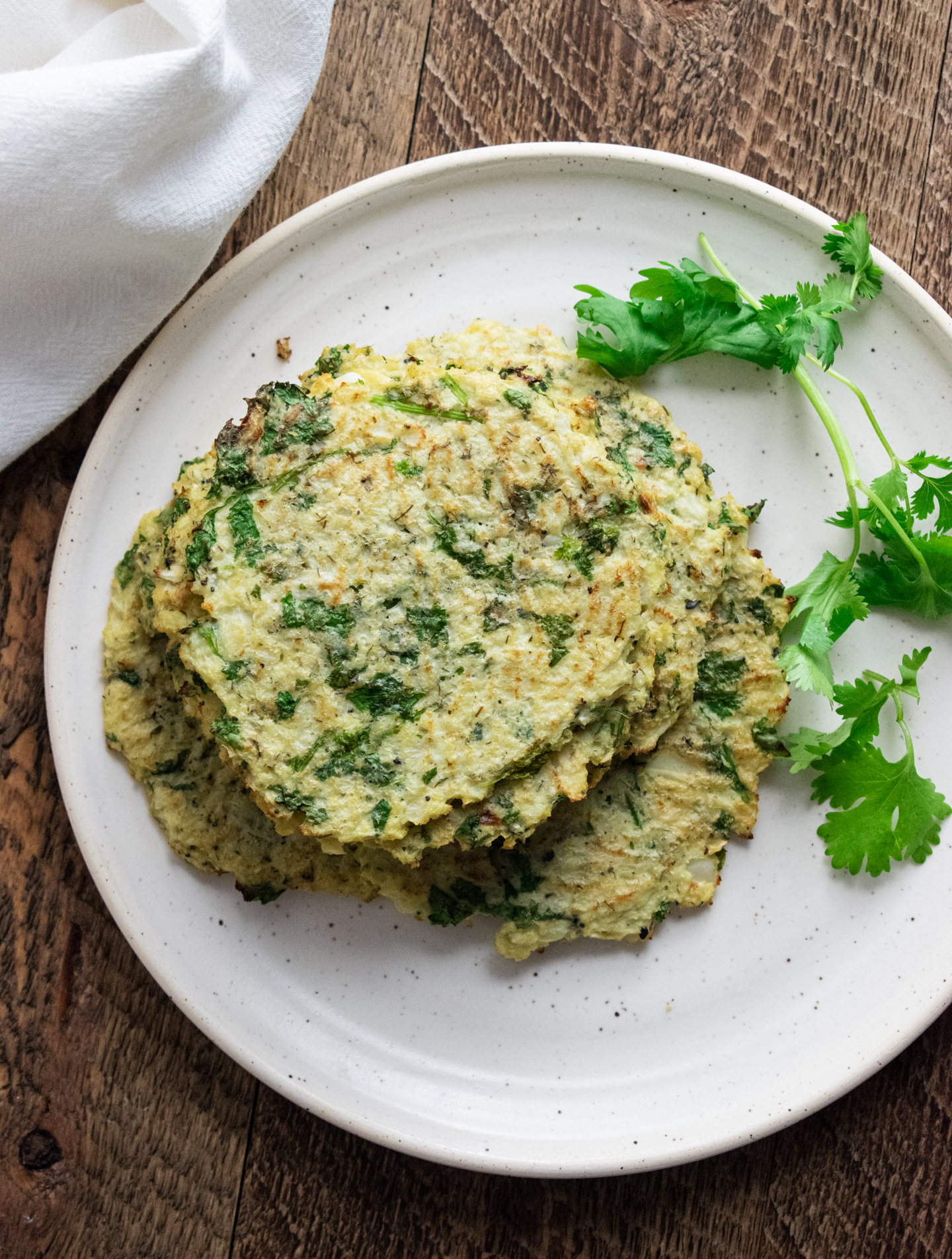 cauliflower egg wraps on a white plate on a wooden board with cilantro leaves and a white napkin