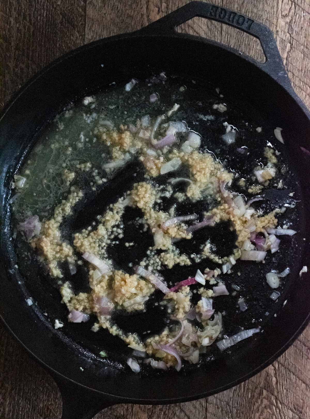 garlic and shallots sauteeing in butter in a cast iron skillet 