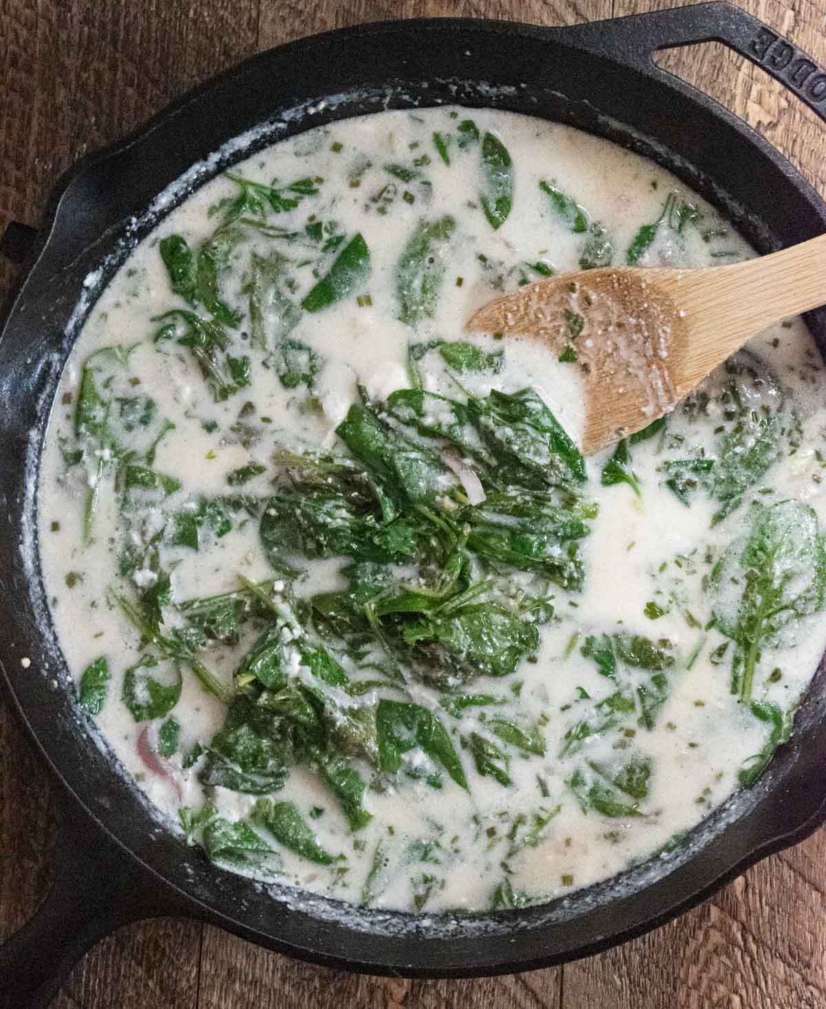 stirring the spinach into the cream sauce with a wooden spoon