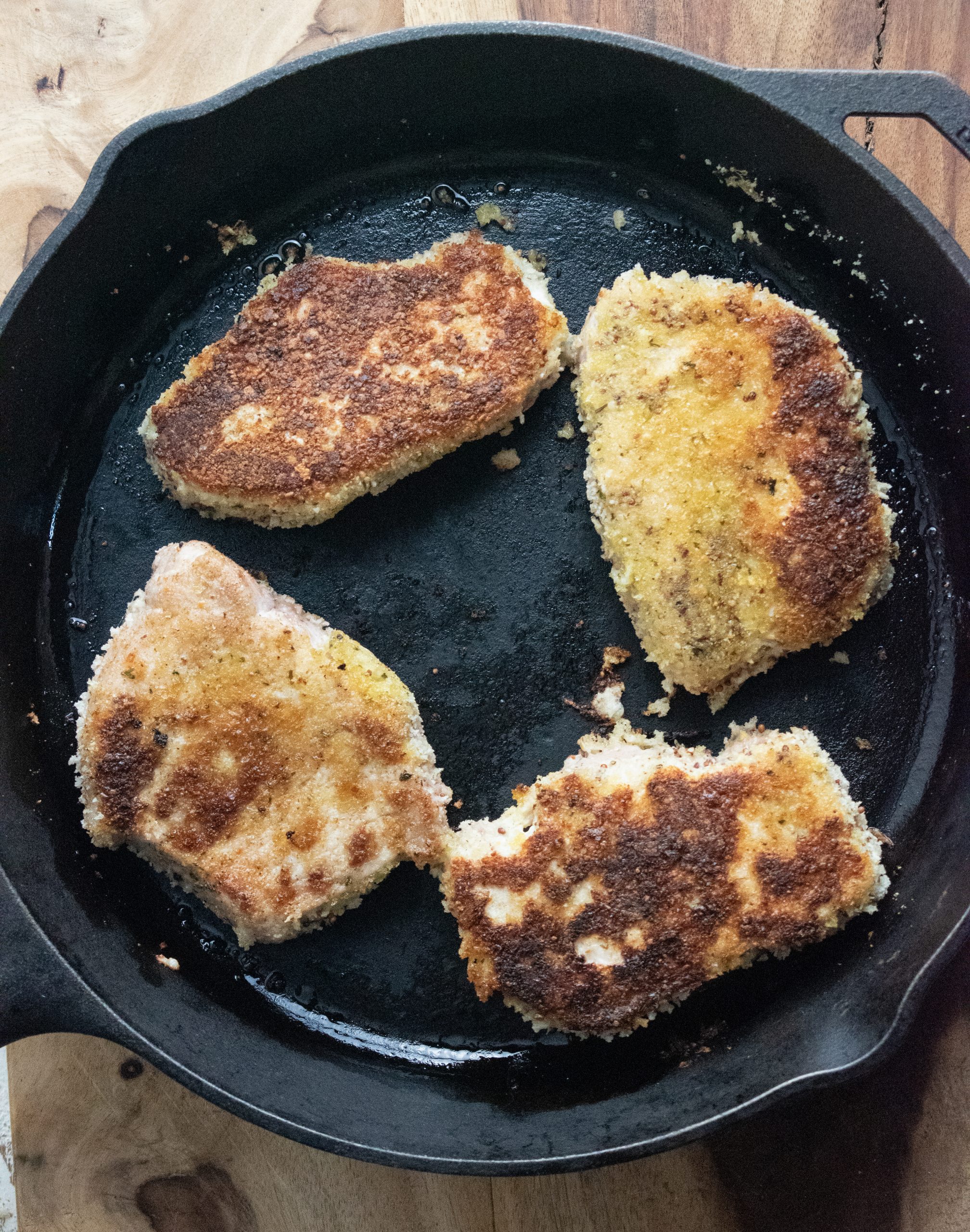 4 porkchops being cooked on a cast iron skillet