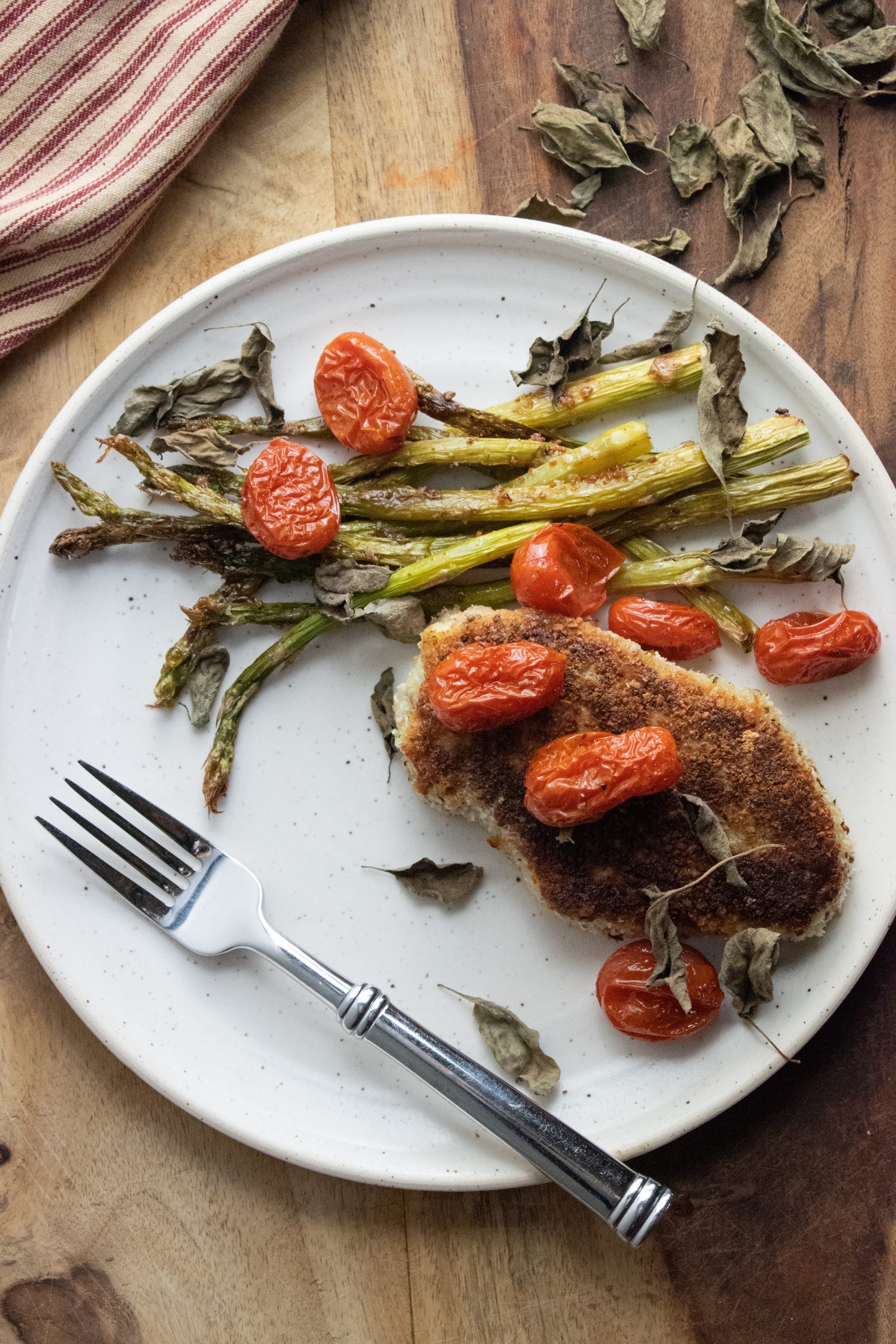 easy pork chops encrusted in a panko mix on a white plate with roasted asparagus and cherry burst tomatoes