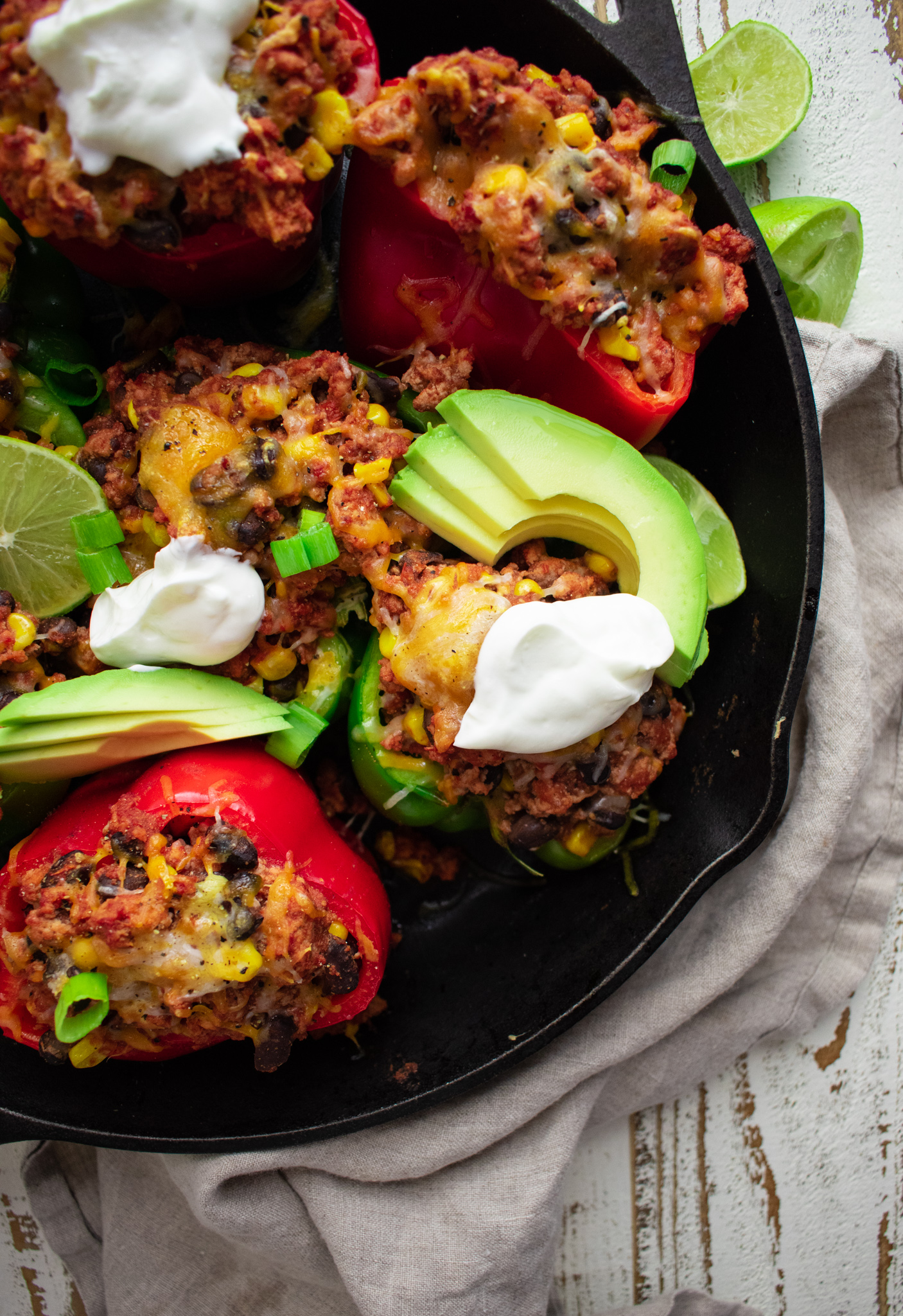 close up of stuffed bell peppers topped with melted cheese, scallions, avocados, and limes