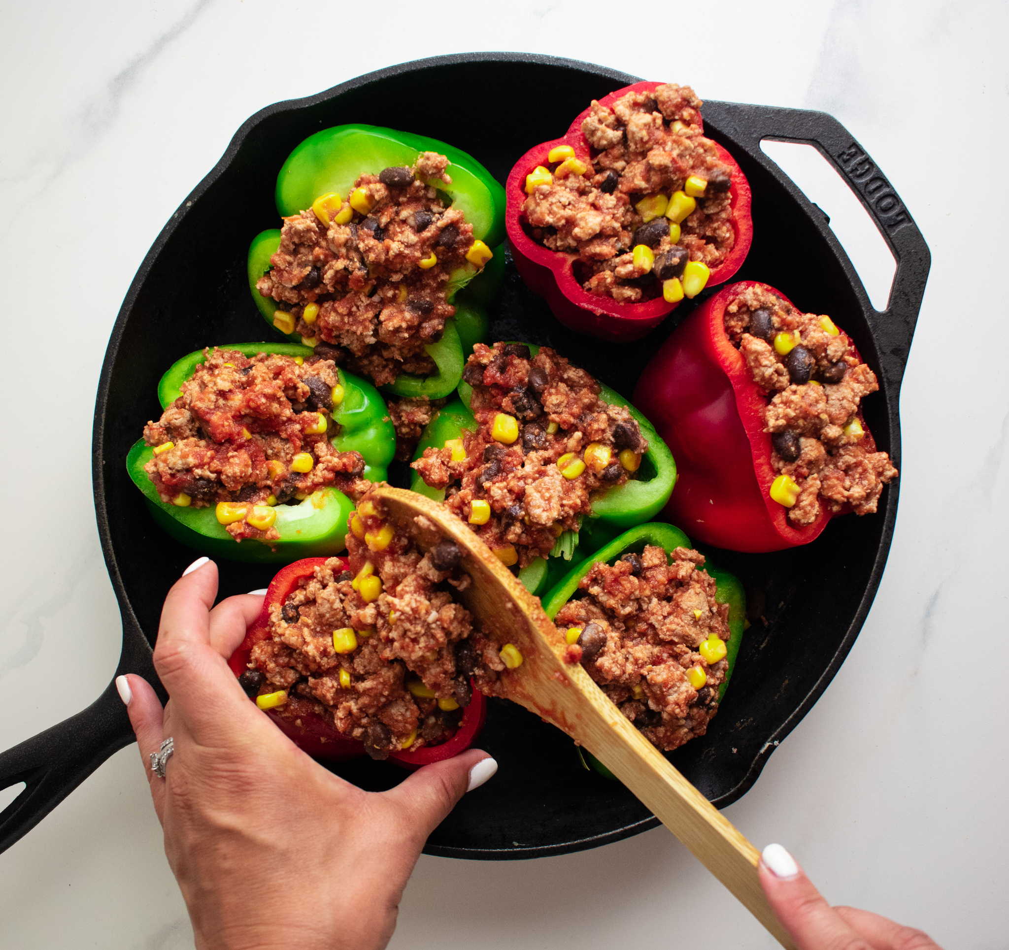 a hand scooping out ground turkey mix using a wooden spoon and filling sliced bell peppers