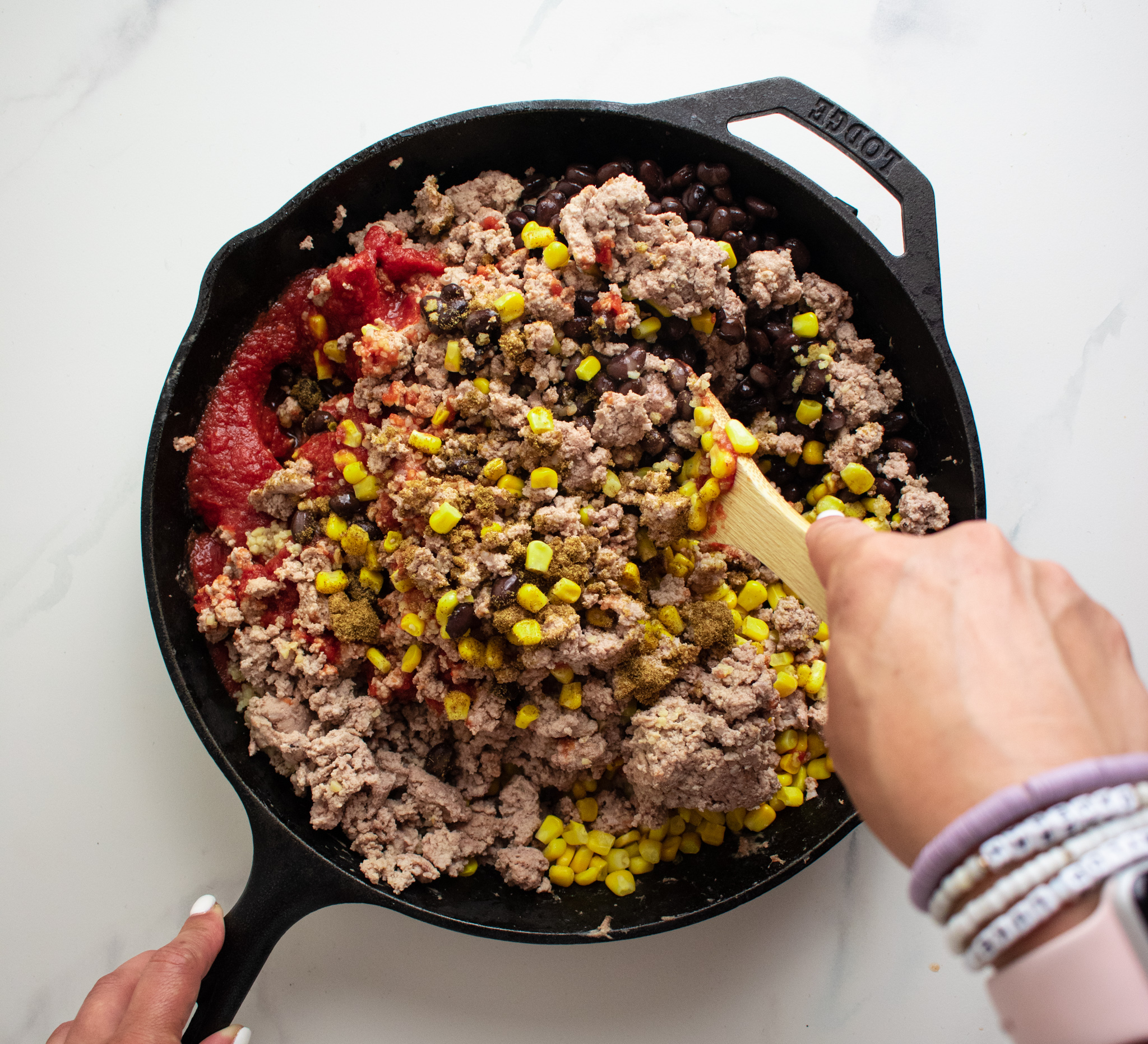 a hand stirring ingredients together in a cast iron skillet using a wooden spoon