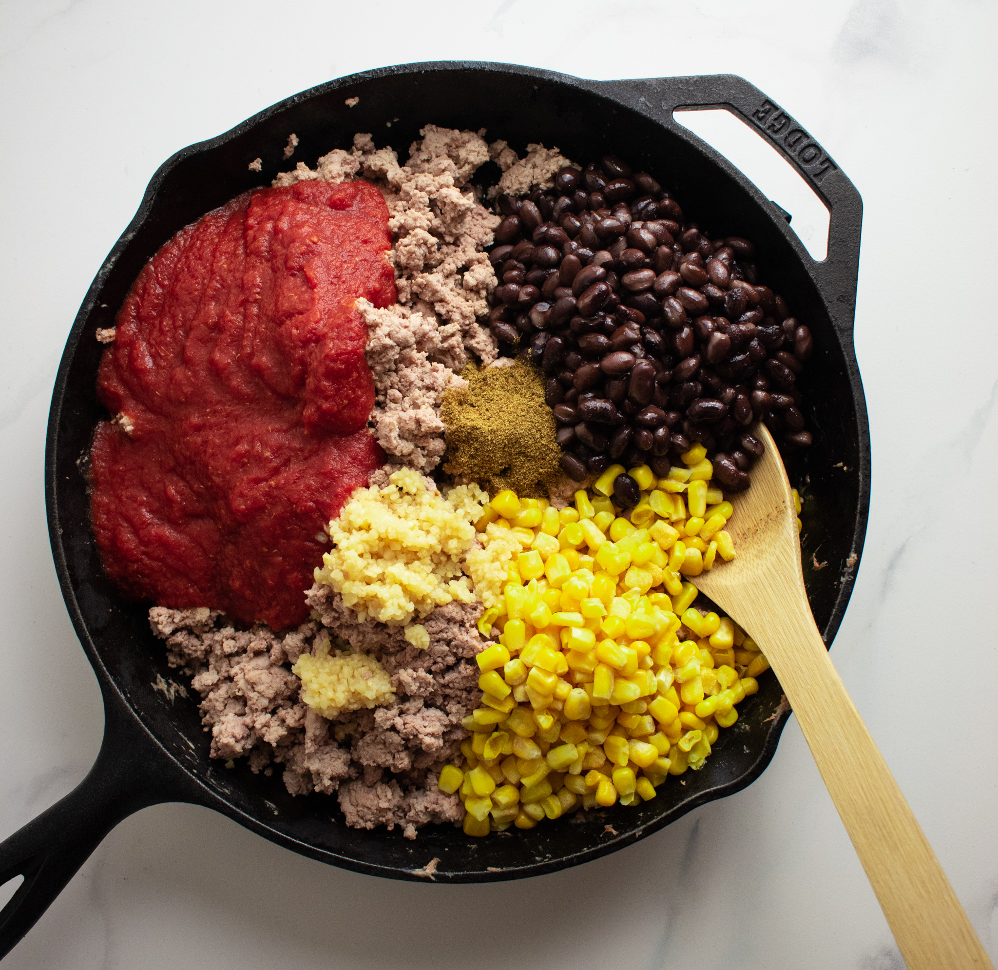 cast iron skillet filled with cooked ground turkey, black beans, corn, tomatoes, cumin, salt, and pepper