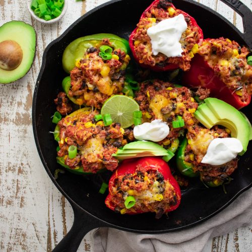 birds eye view of stuffed peppers in a cast iron skillet topped with avocados scallions and limes