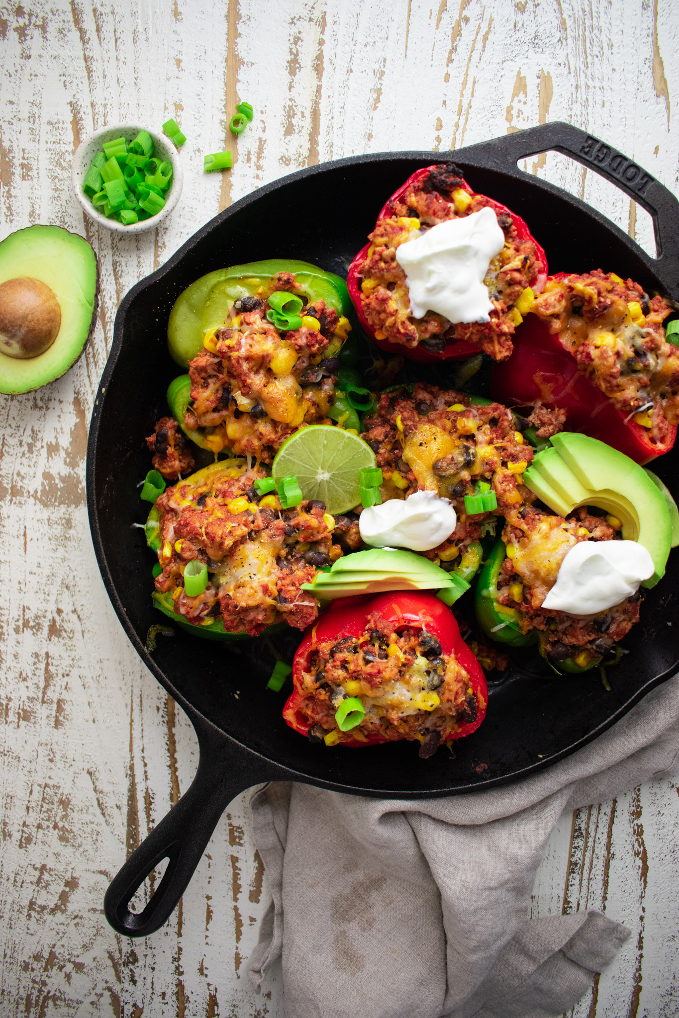 birds eye view of stuffed peppers in a cast iron skillet topped with avocados scallions and limes