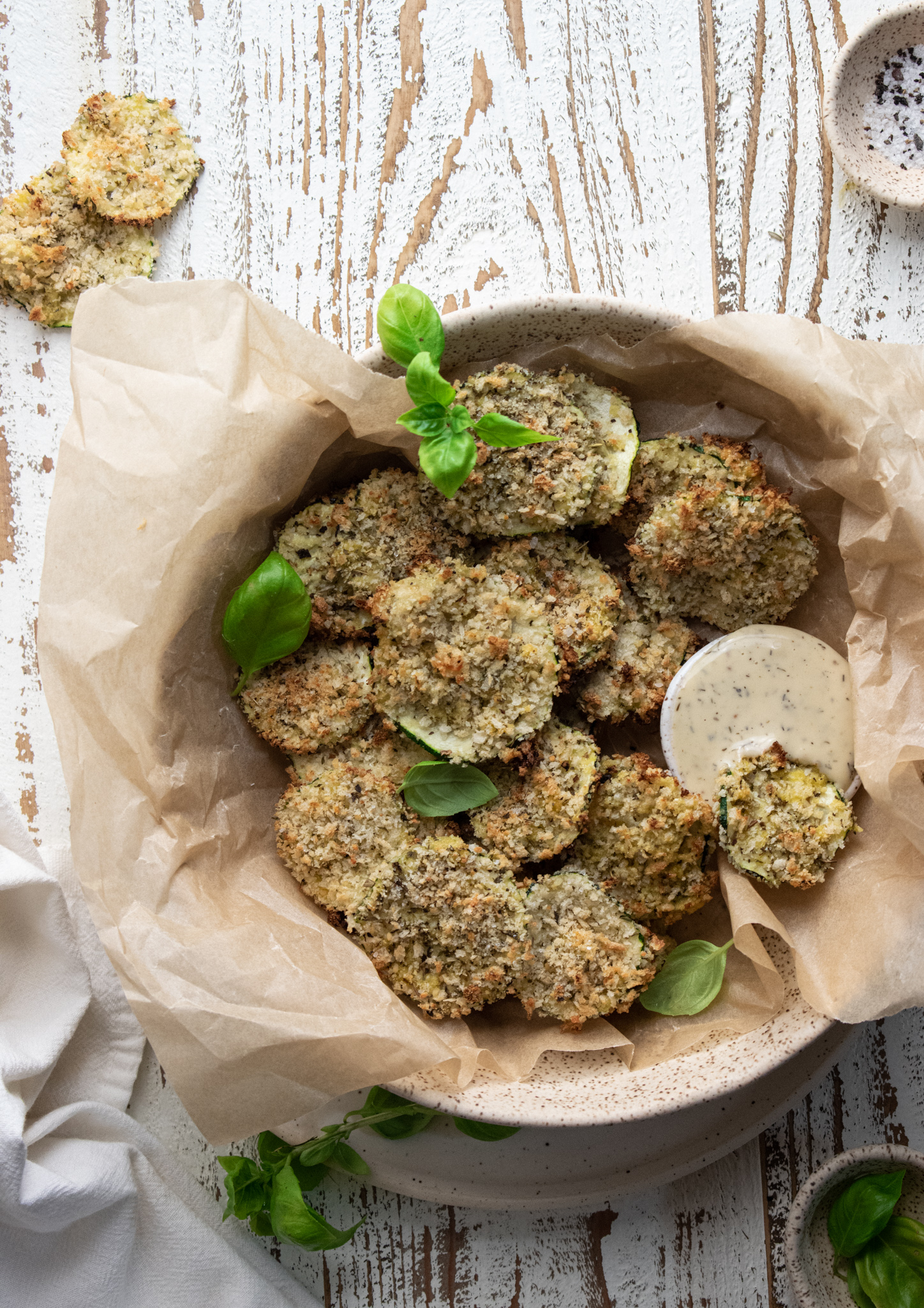 baked zucchini chips in a bowl filled with parchment paper on a wooden white board