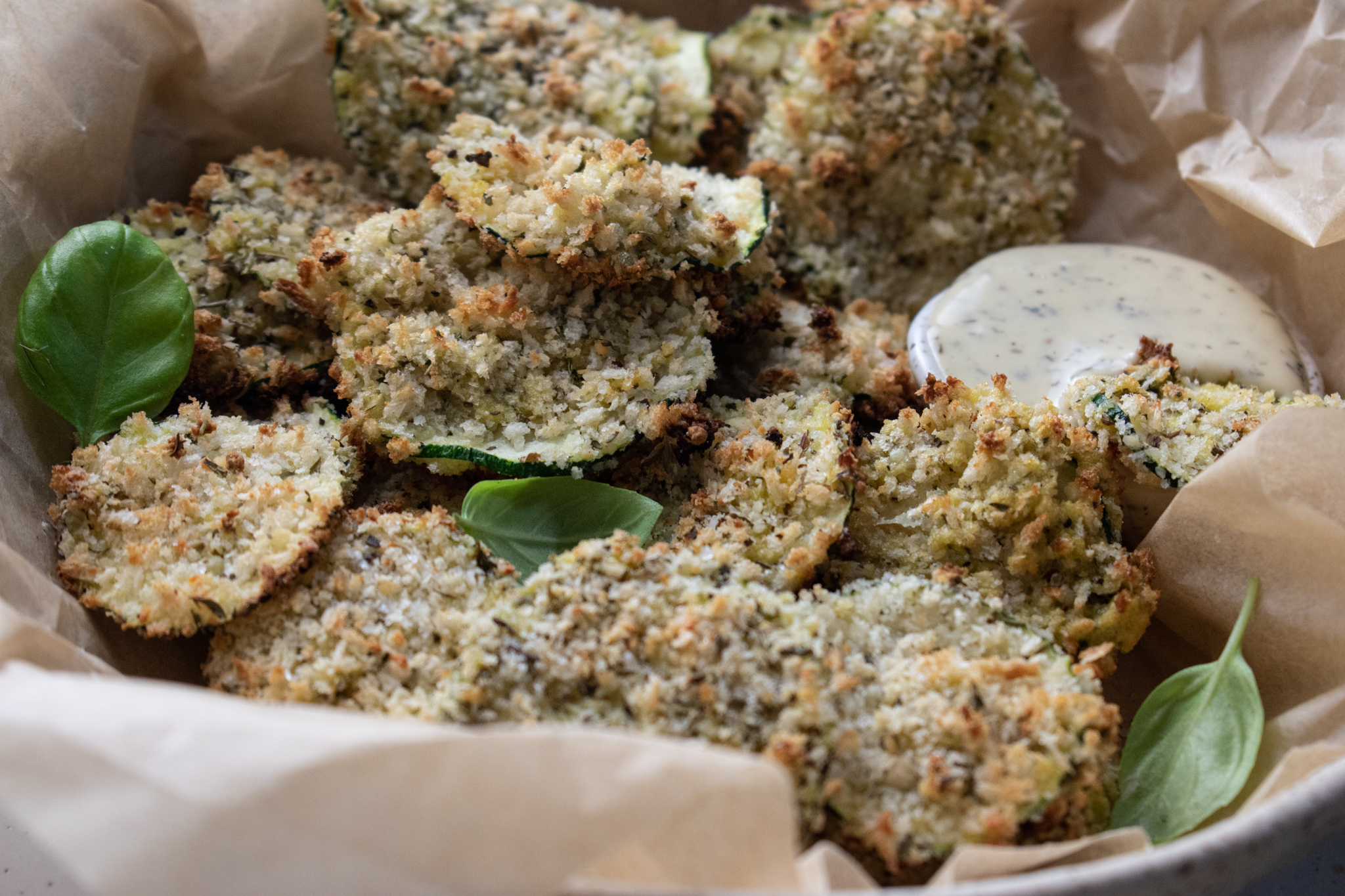 close up of oven baked zucchini chips in a bowl filled with parchment paper