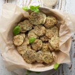 oven baked zucchini chips in a bowl filled with parchment paper on a white wooden board