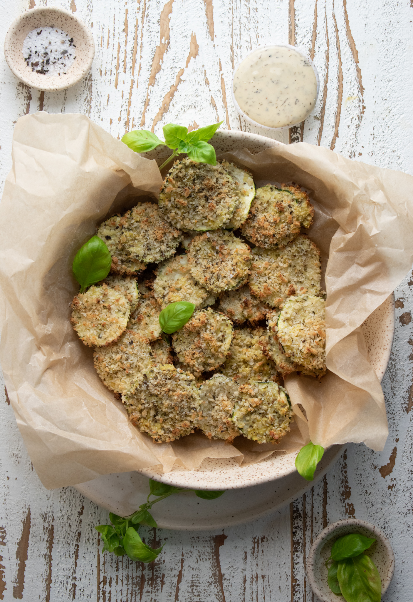 oven baked zucchini chips in a bowl filled with parchment paper on a white wooden board