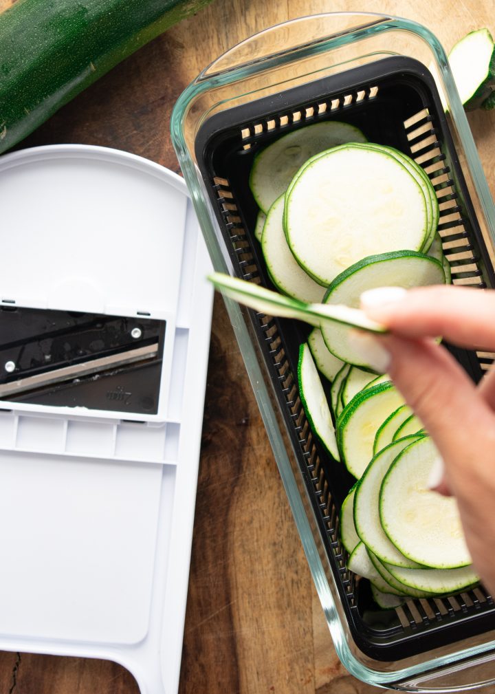 mandolin slicer and a hand holding very thin zucchini chips