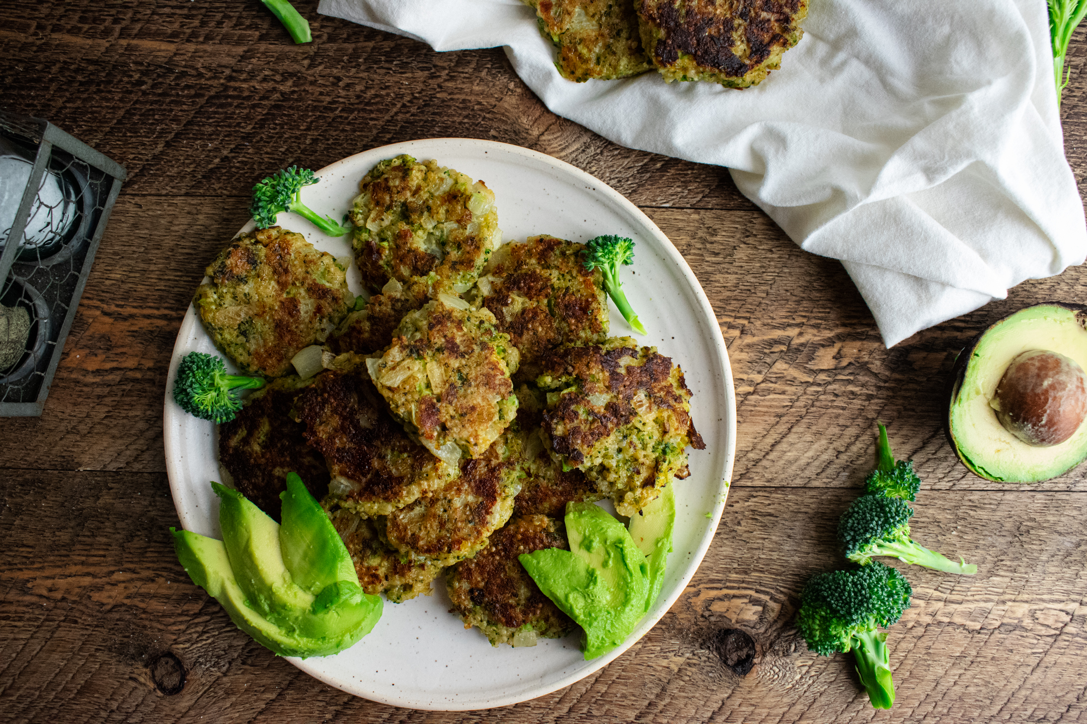 veggie quinoa patties on a white serving plate with avocado and broccoli on top of a wooden board