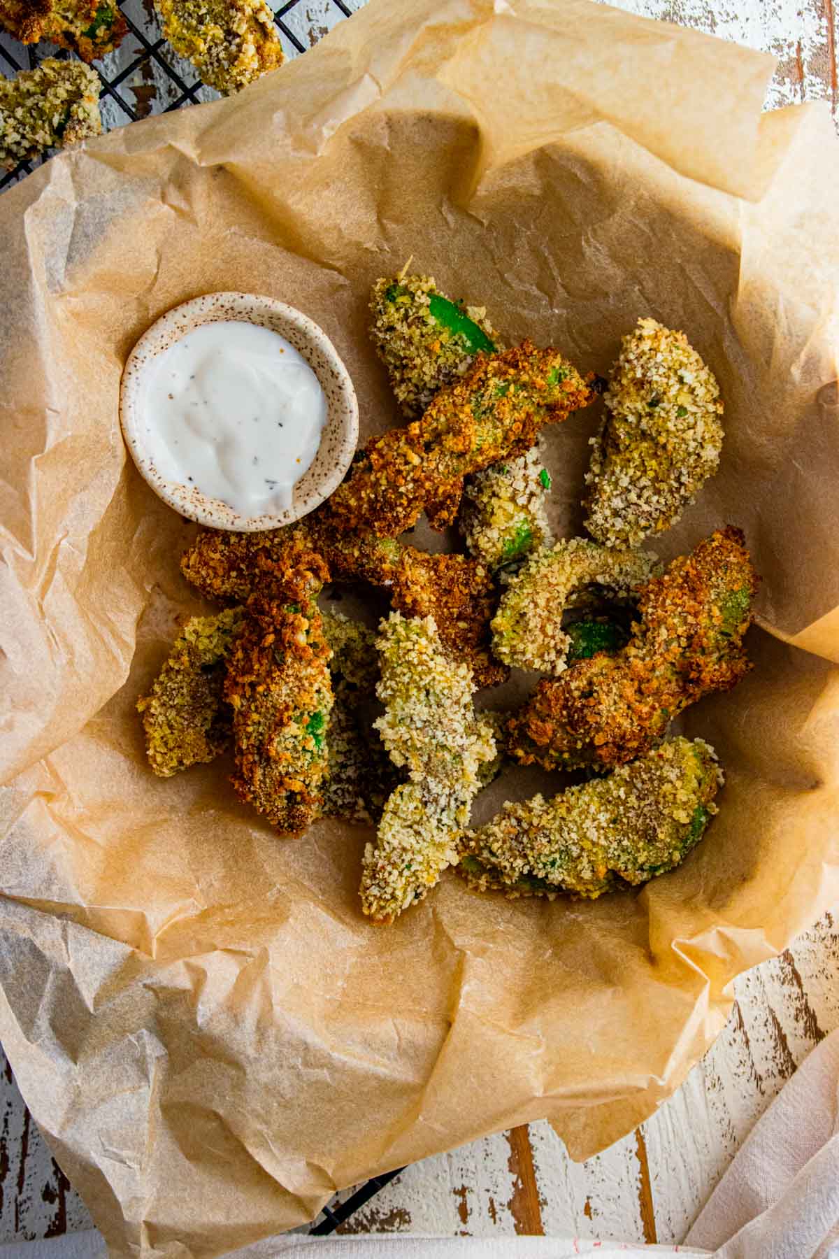 A birds-eye view of avocado fries in a bowl with parchment paper and a dipping sauce. 