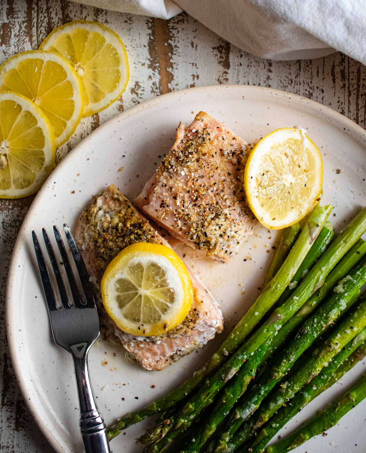 salmon with lemon and butter on a white plate with asparagus and lemon slices