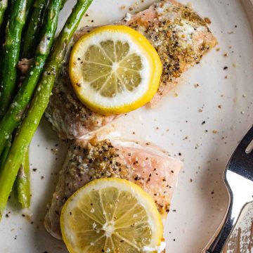 easy baked salmon with lemon and butter on a white plate with asparagus and lemon slices