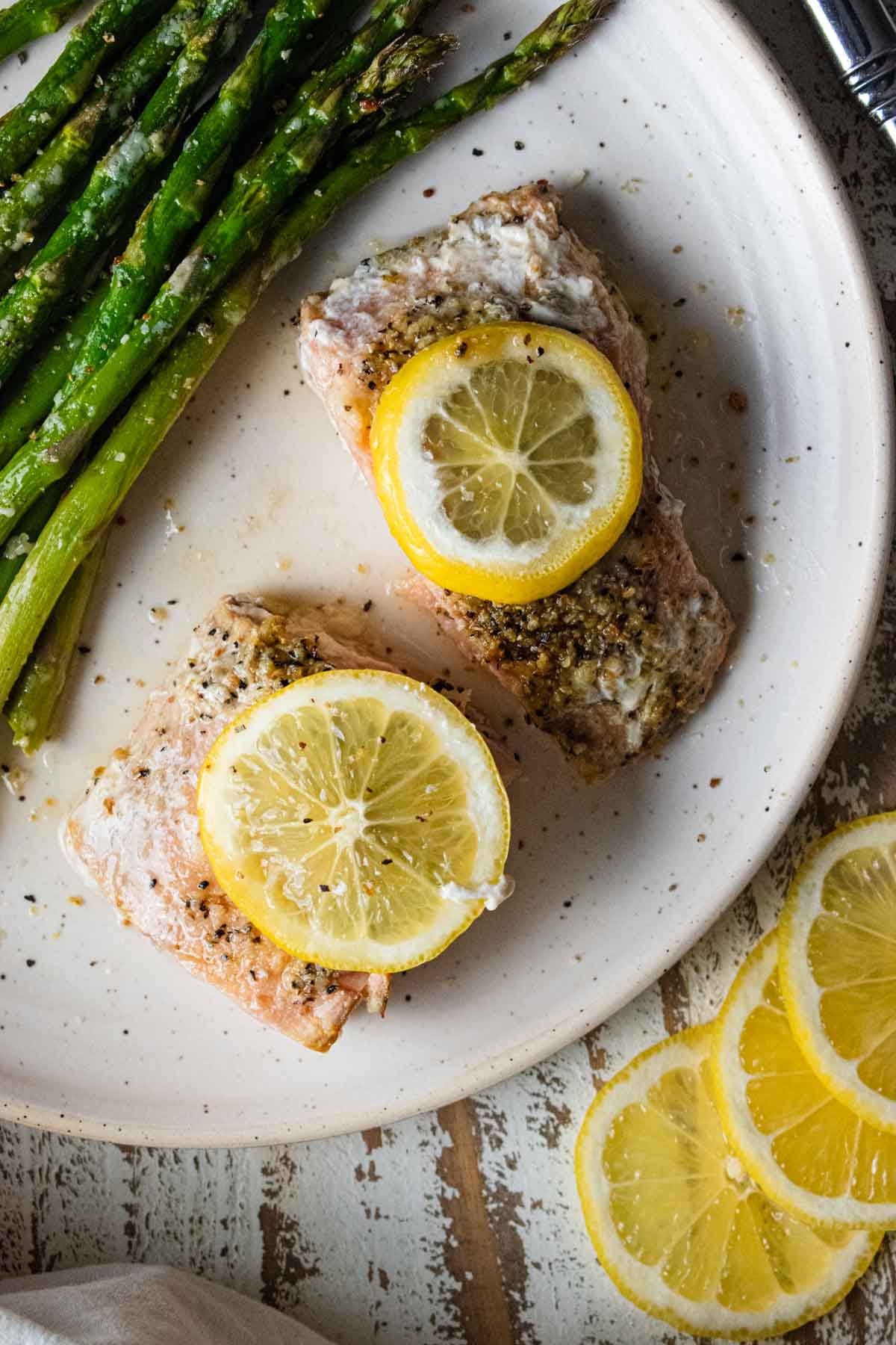 close up of easy baked salmon with lemon and butter on a white plate with lemon slices and asparagus