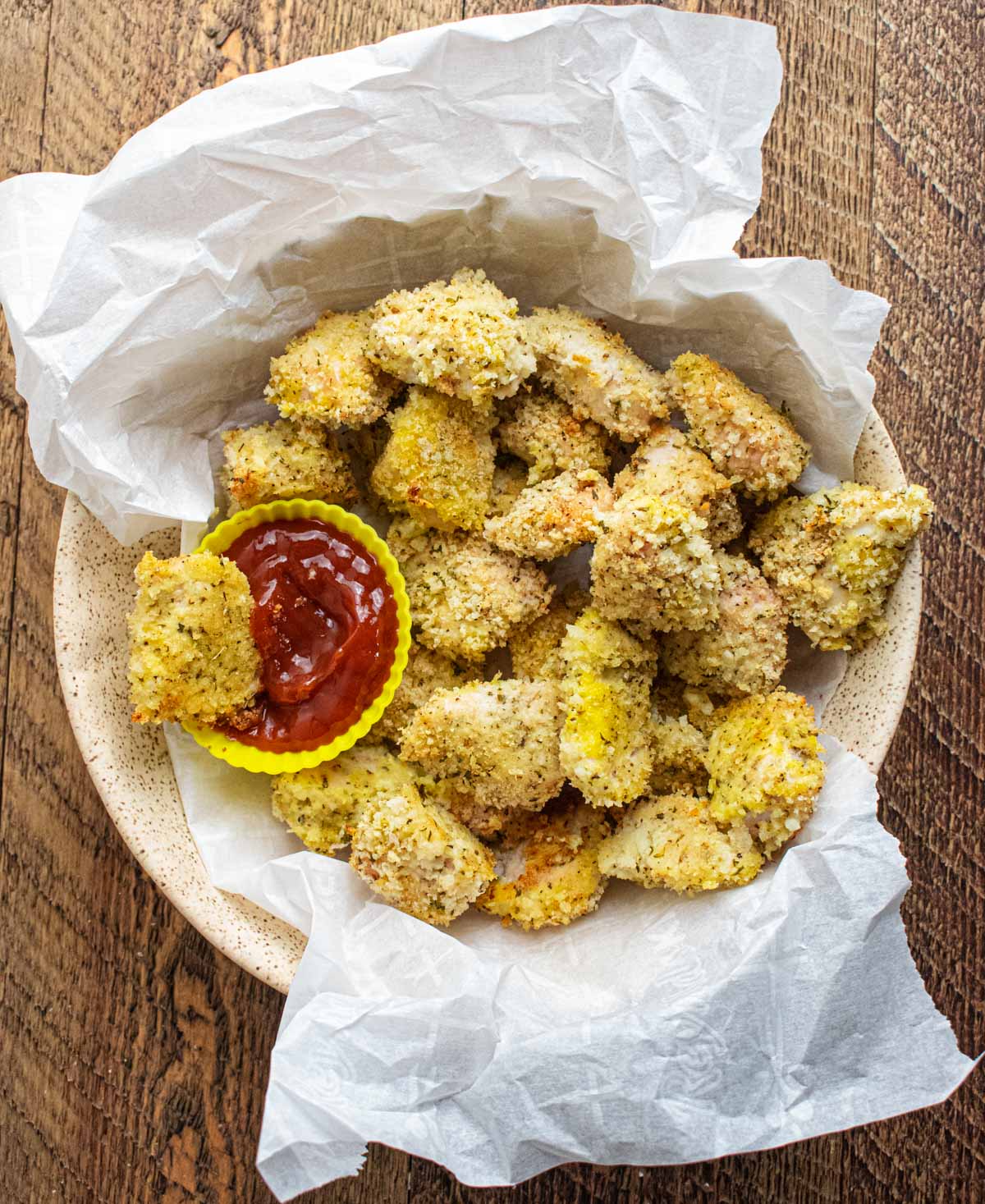 homemade baked chicken nuggets in a bowl with a tiny cup of ketchup