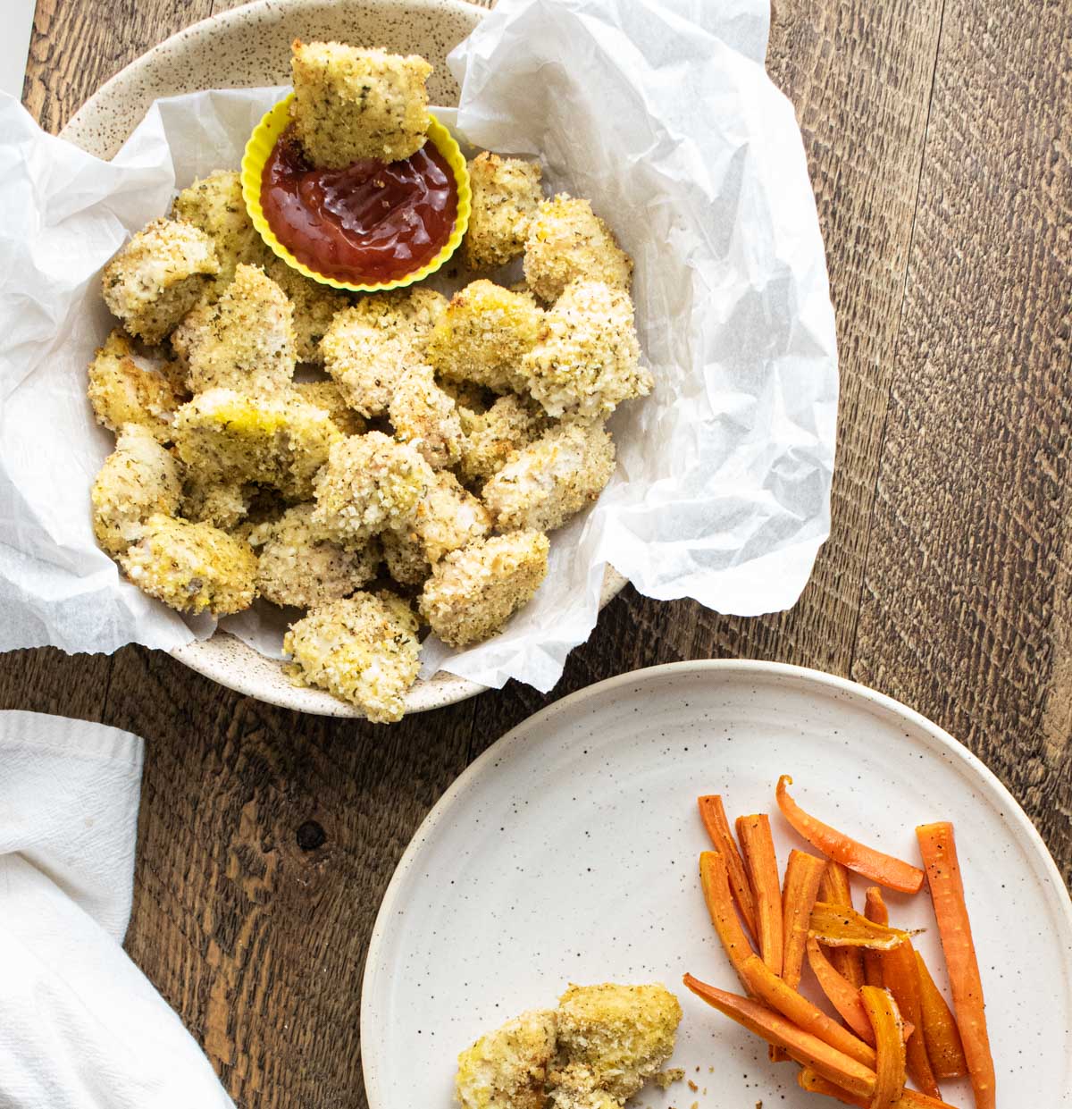 homemade baked chicken nuggets with honey glazed carrots on white plates on a wooden table
