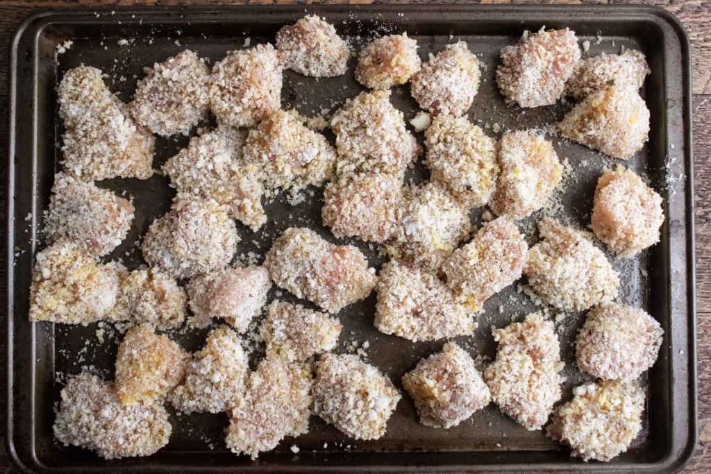 crispy chicken pieces lined on a baking sheet right before cooking to make homemade baked chicken nuggets