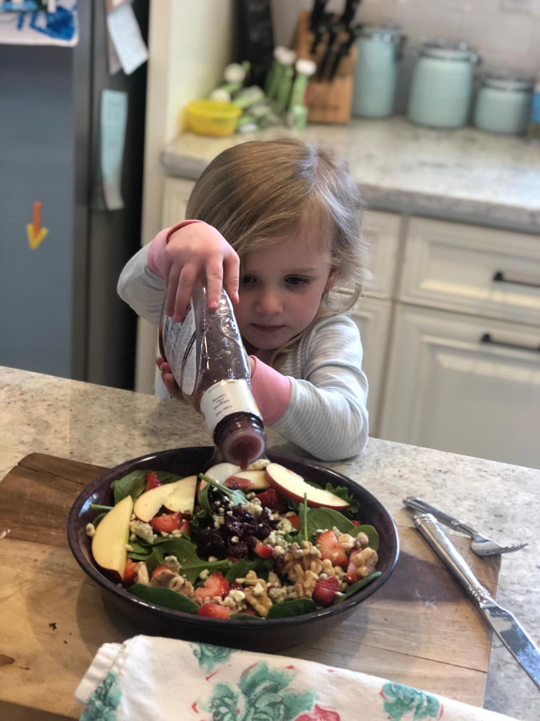 little blonde girl putting salad dressing on a salad