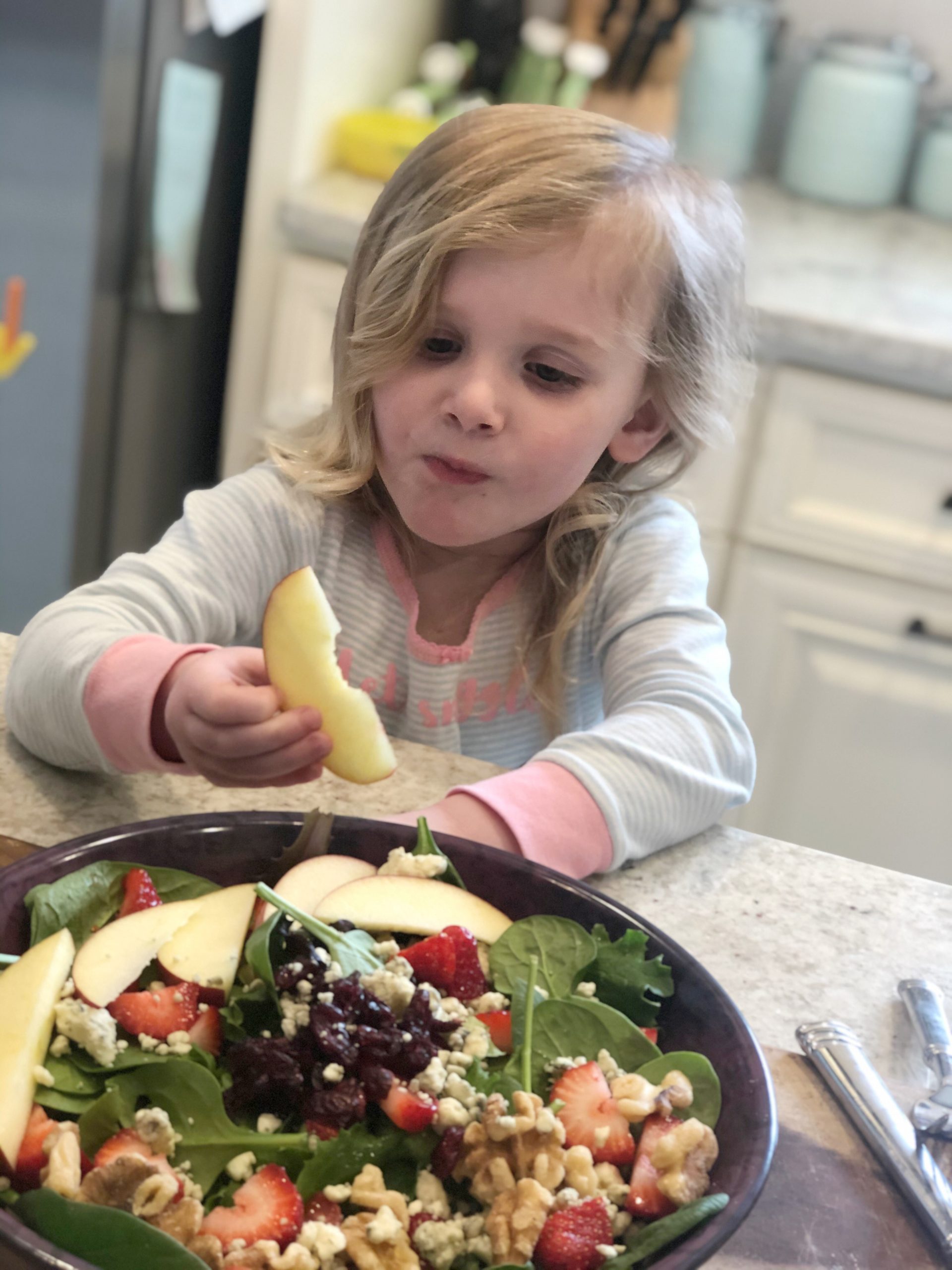 little blonde girl eating an apple off a salad