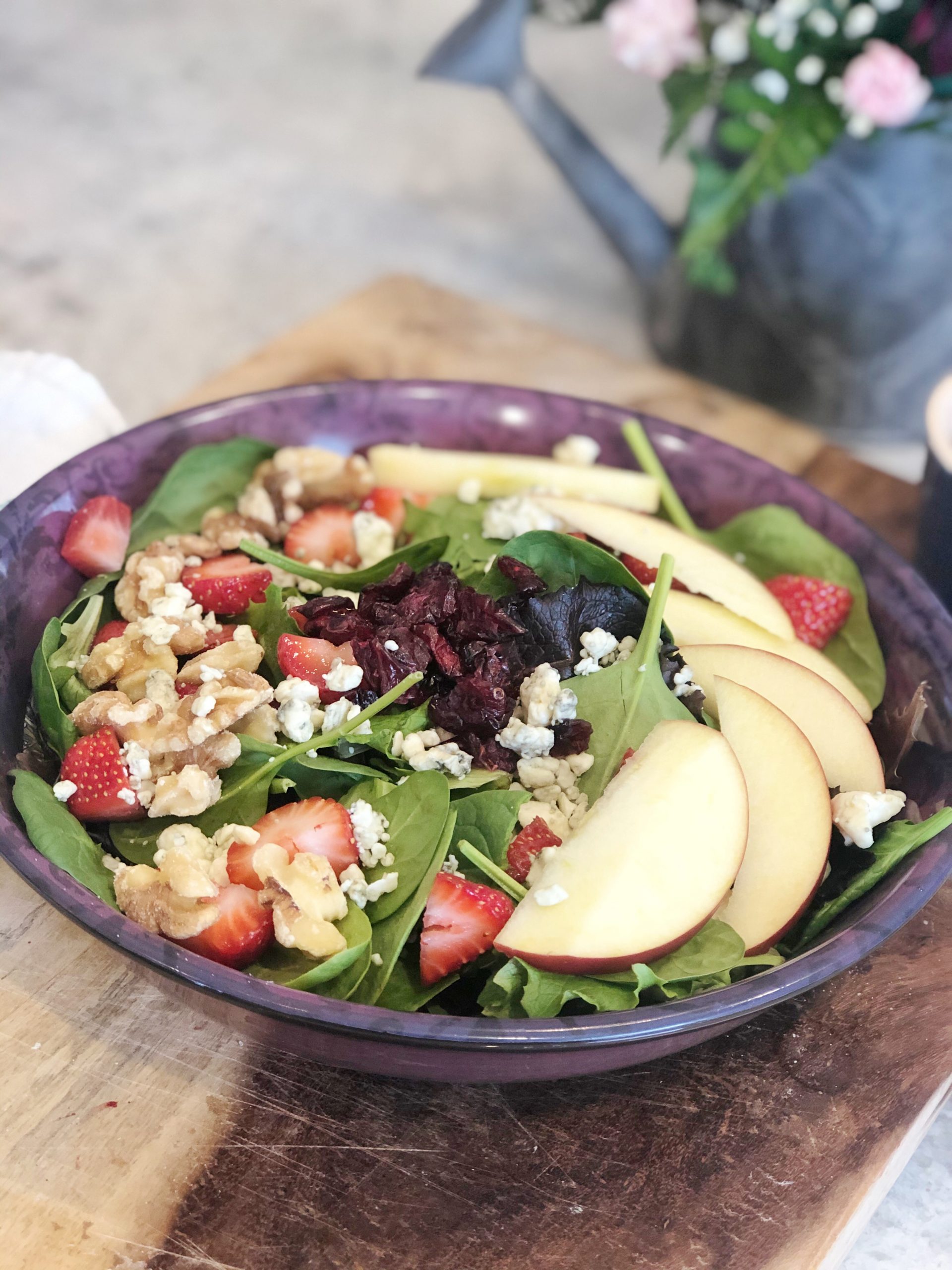 close up of salad with spinach, apples, raisins, walnuts, strawberries, and bleu cheese