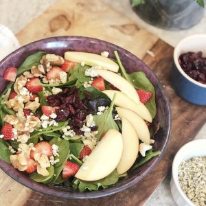 a salad made with spinach, apples, raisins, bleu cheese, strawberries, and walnuts