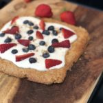 almond cookie tart with fruit on a wooden cutting board with strawberries in the background
