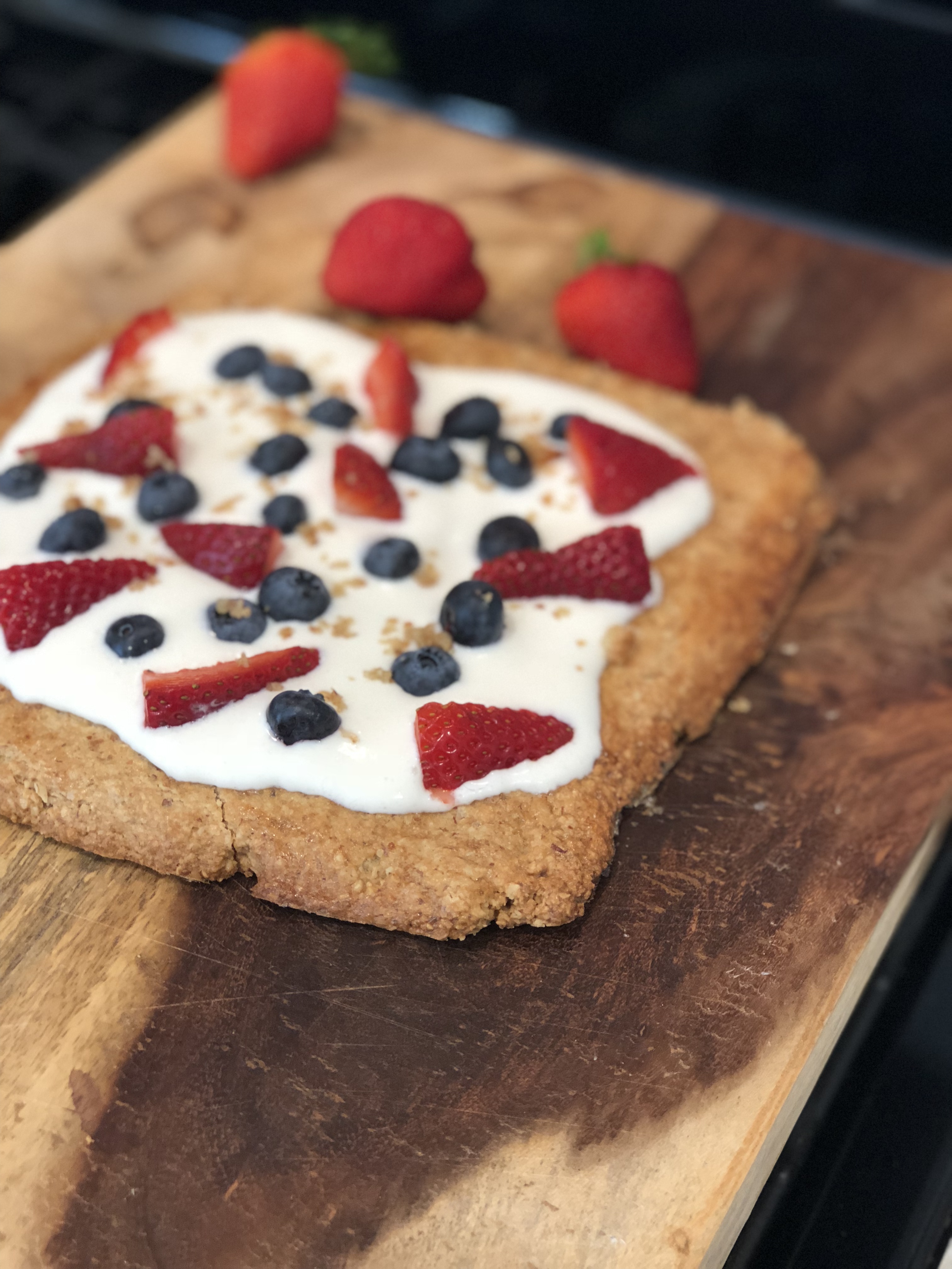 almond cookie tart with fruit on a wooden cutting board with strawberries in the background