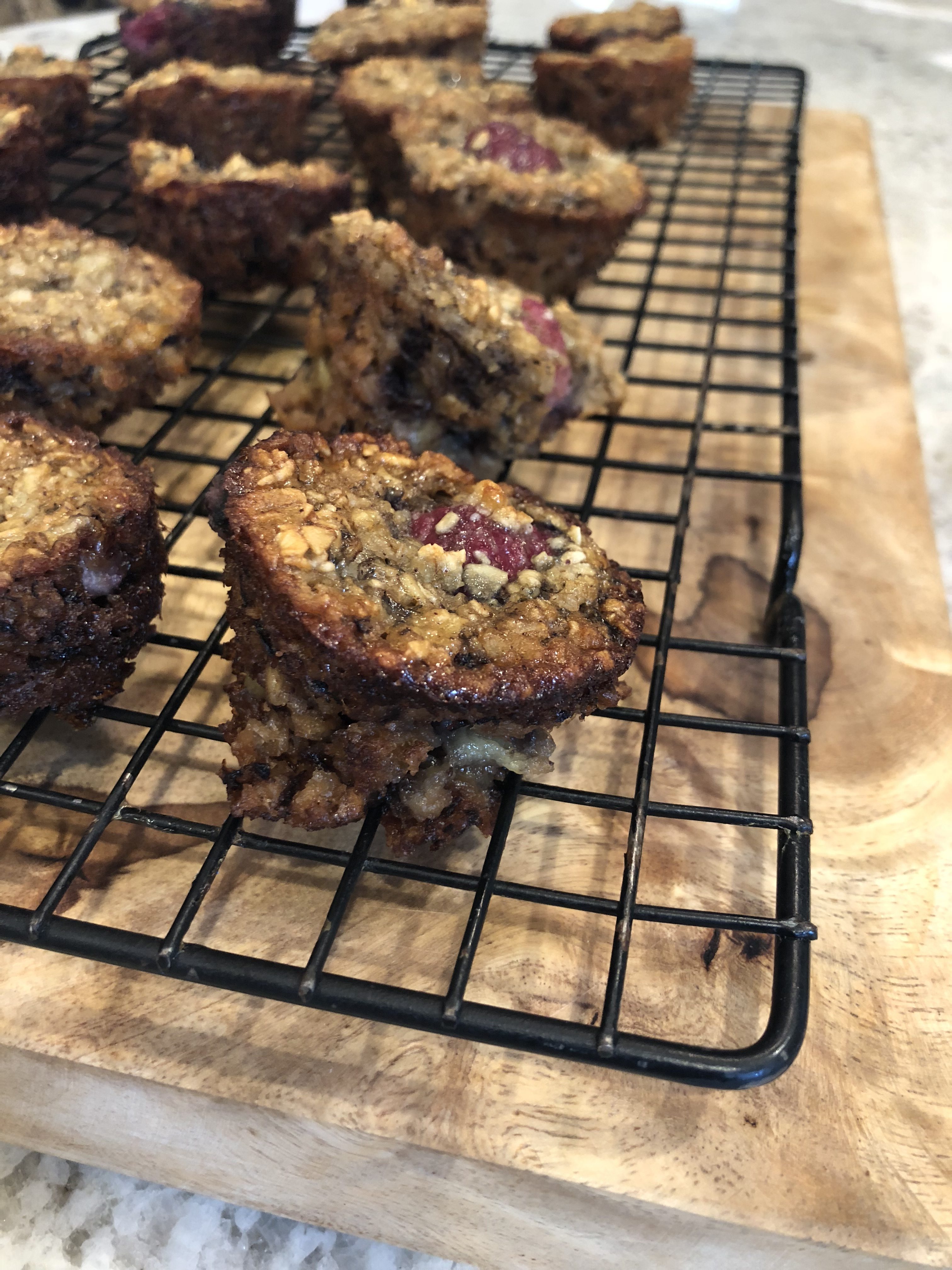 close up of raspberry banana mini muffins on a cooling rack sitting on a wooden board