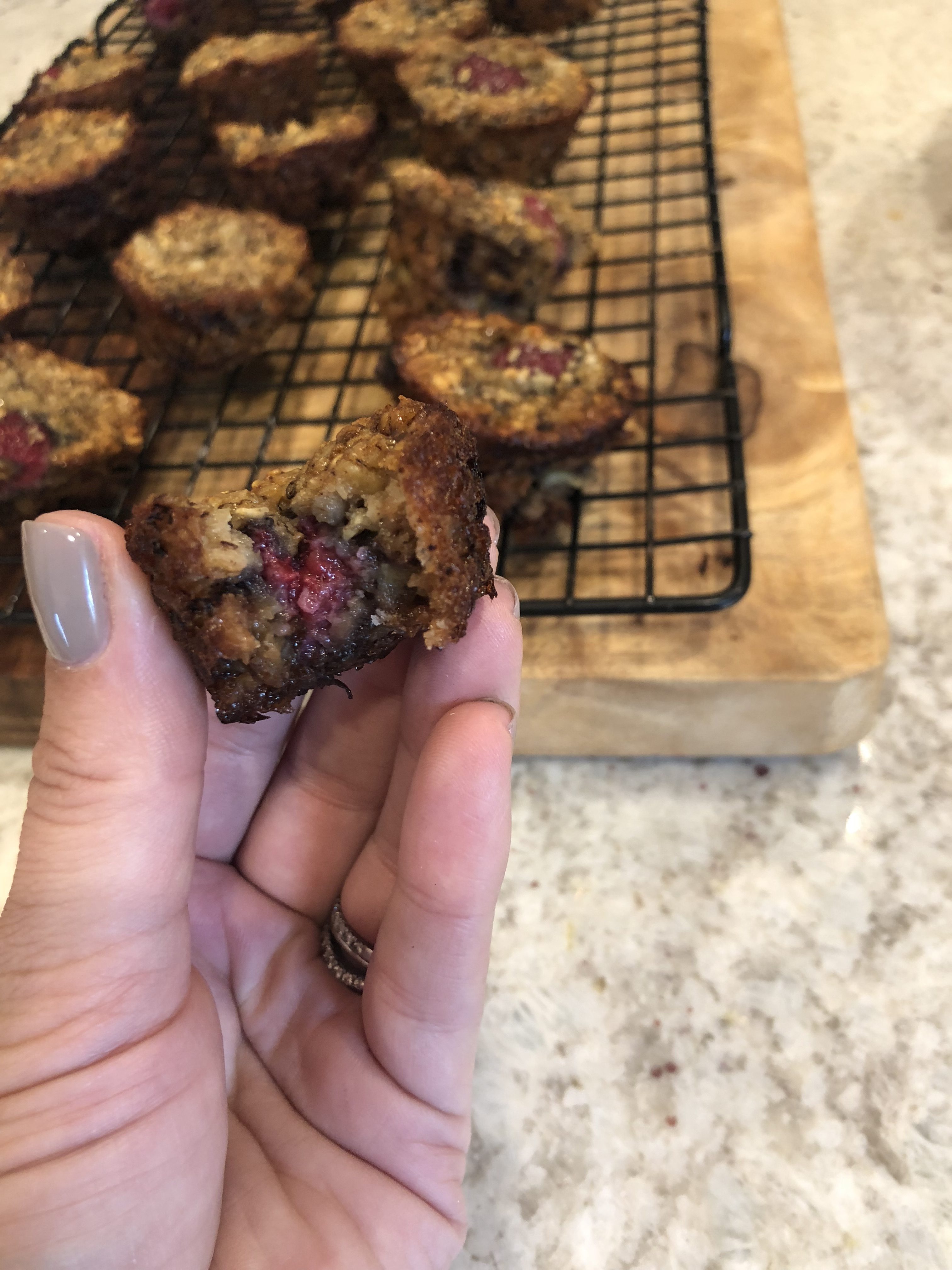 raspberry banana mini muffins on a cooling rack on a wooden board with a hand holding one with a bite out of it