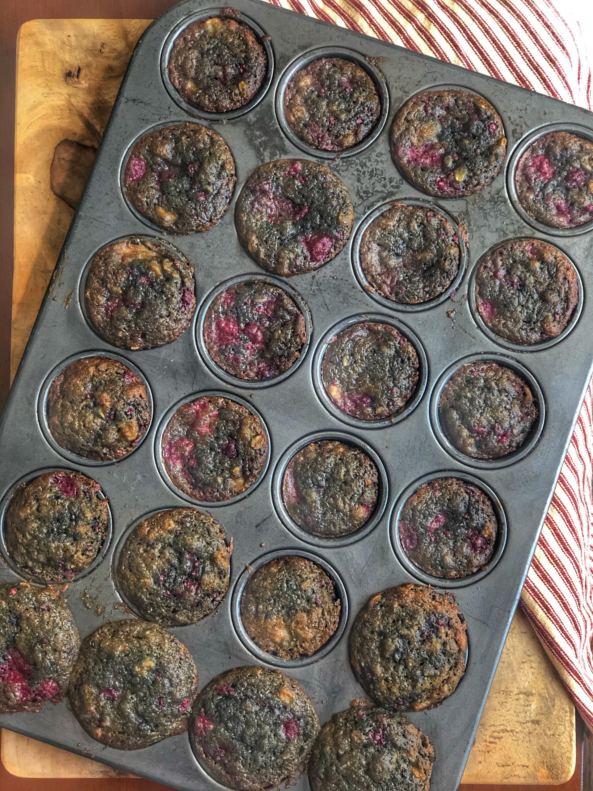 raspberry banana mini muffins in a mini muffin tin on a wooden board