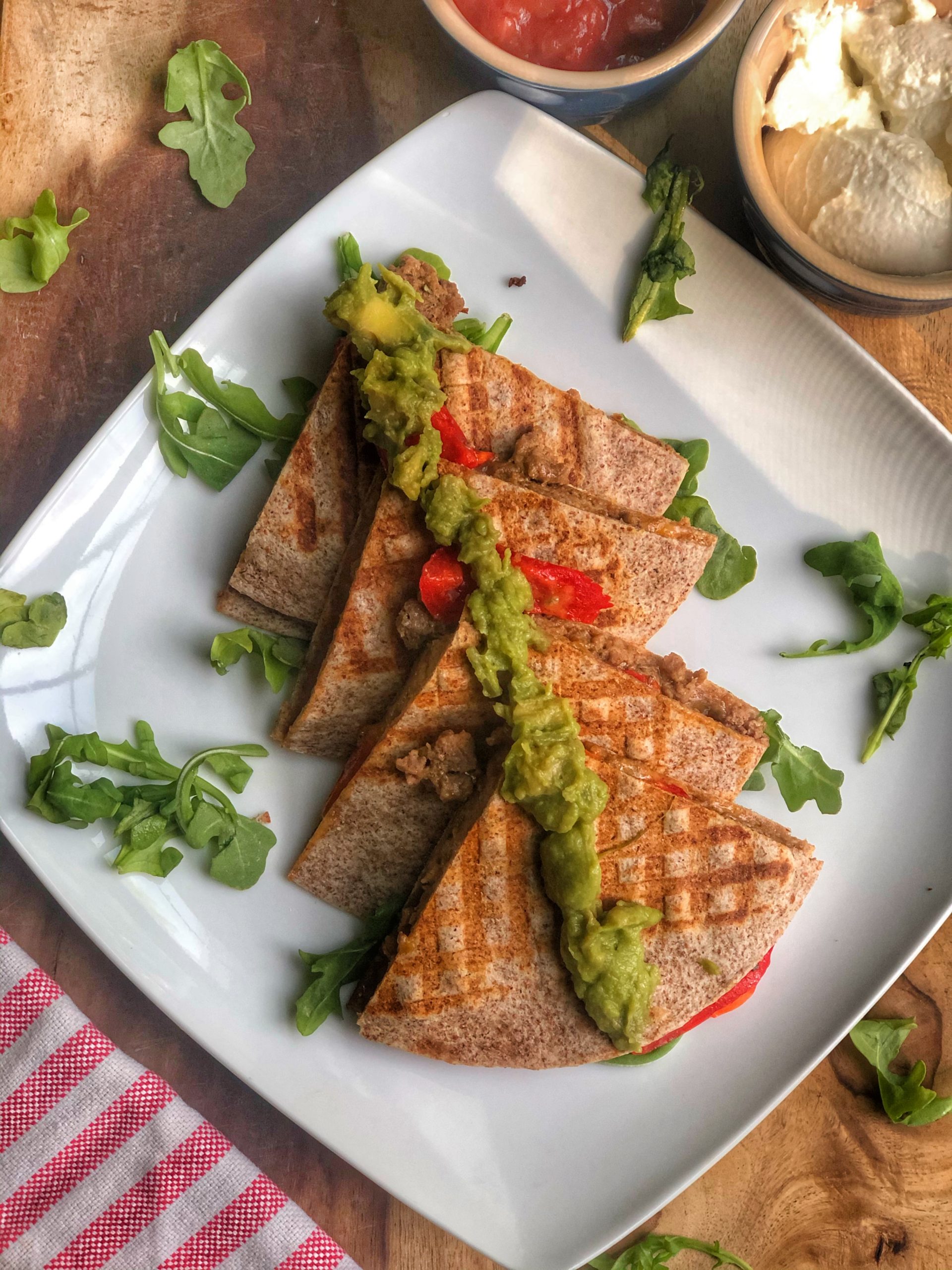 quesadillas on a white plate on a wooden board with salsa and plain greek yogurt for dipping