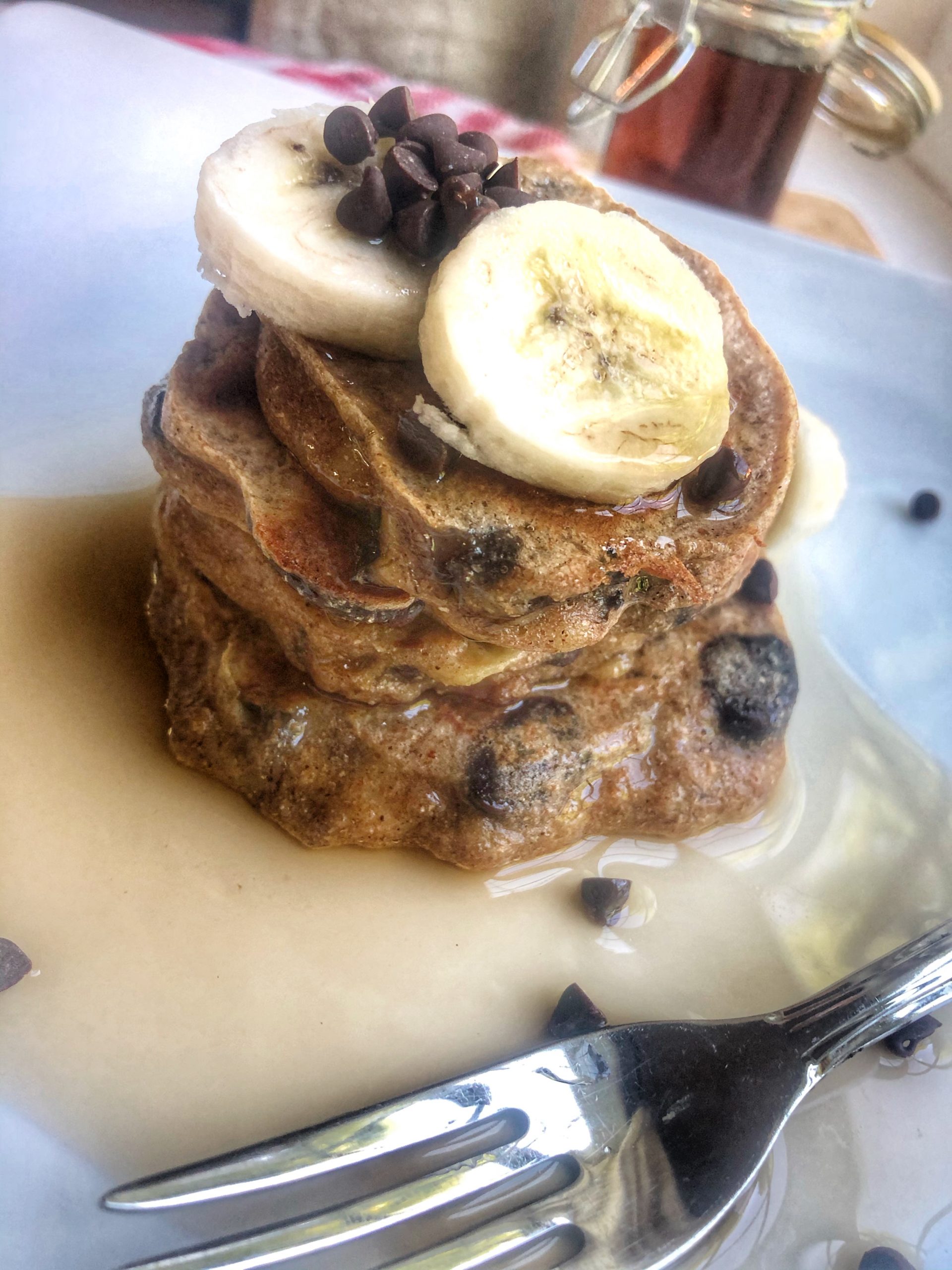 close up of banana chocolate chip whole wheat pancakes on a white plate with a silver spoon
