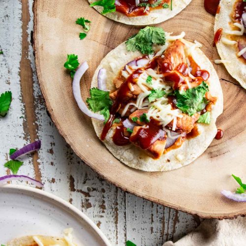 bbq chicken flatbread on a wooden plate with red onion and cilantro sprinkled on top