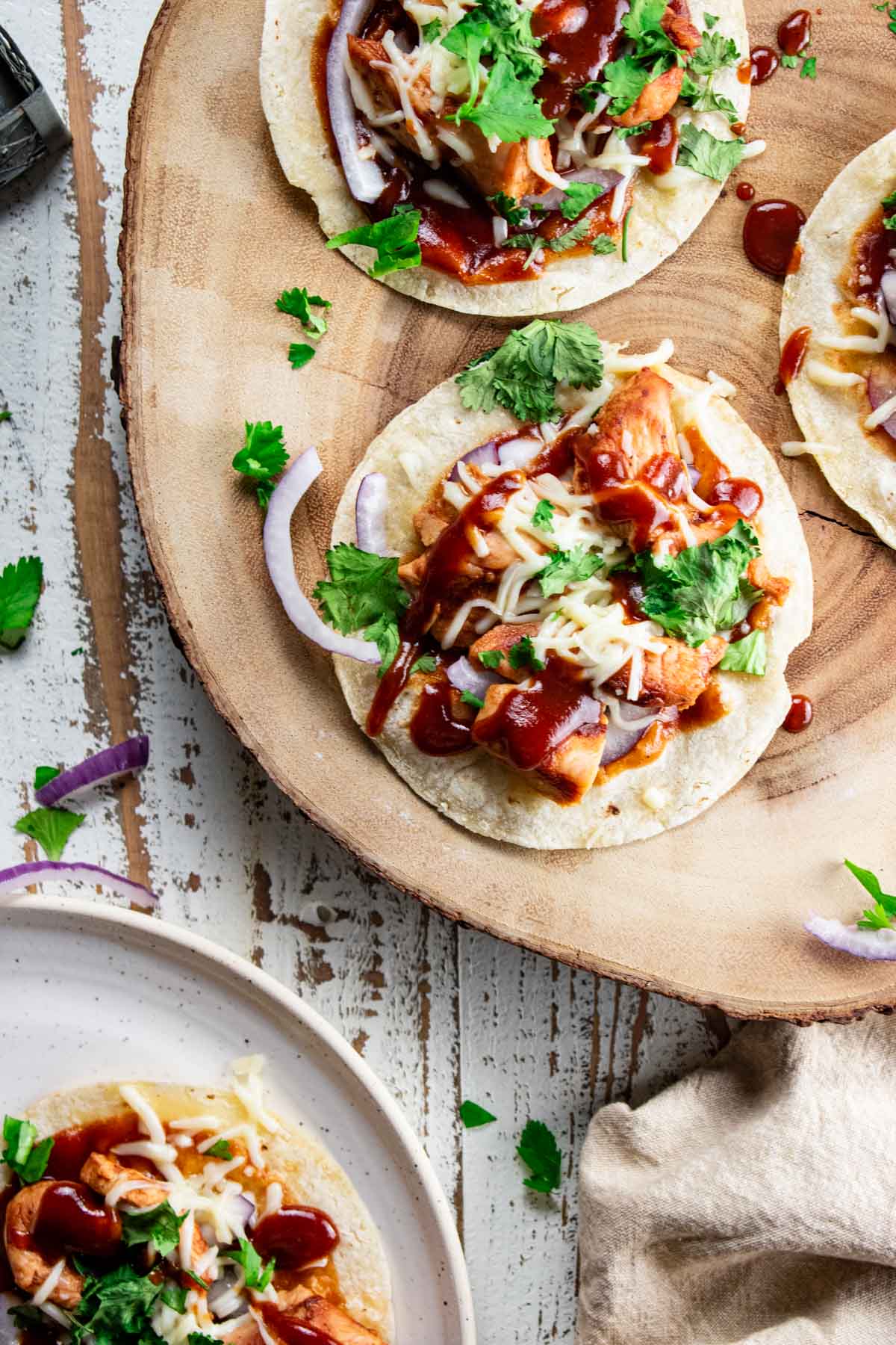 bbq chicken flatbread on a wooden plate with red onion and cilantro sprinkled on top