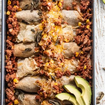 ground turkey enchiladas topped with sliced avocado in a deep dish on a white wooden table