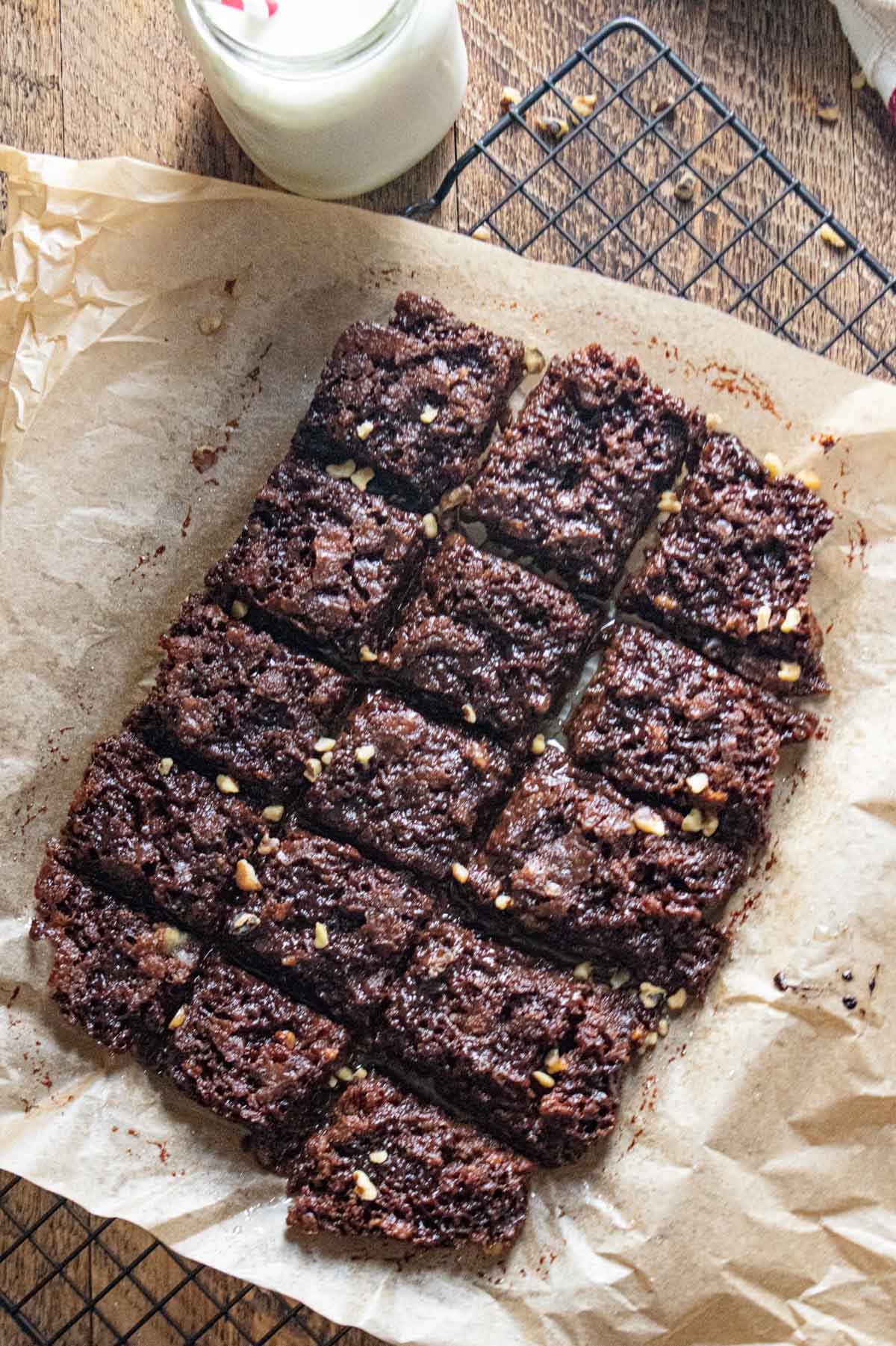 birds eye view of gluten free dairy free brownies on parchment paper on top of a wooden table with a glass of milk