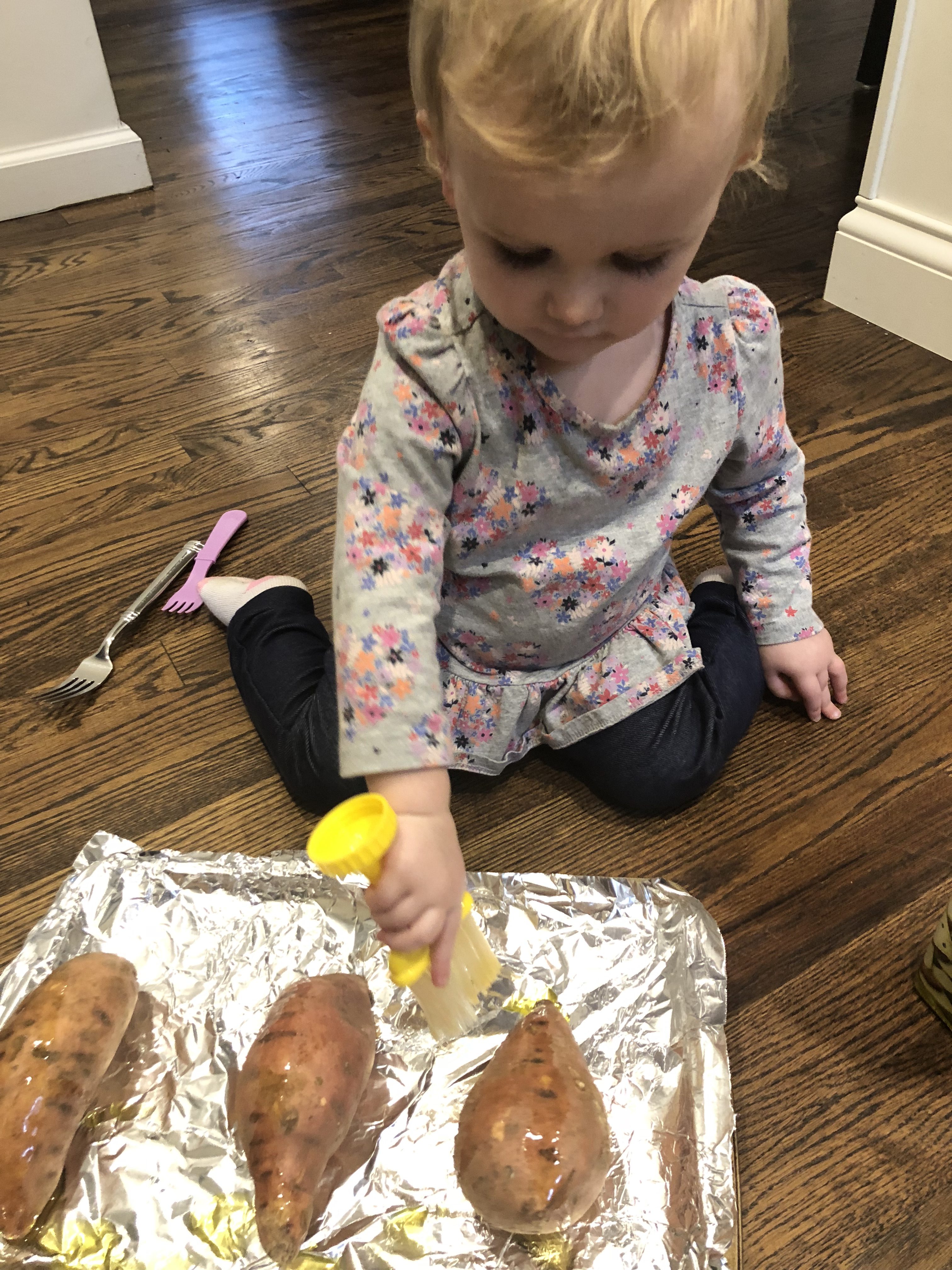 little blonde girl brushing oil onto sweet potatoes