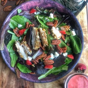 homemade strawberry vinaigrette dressing pictured with a salad on a wooden board