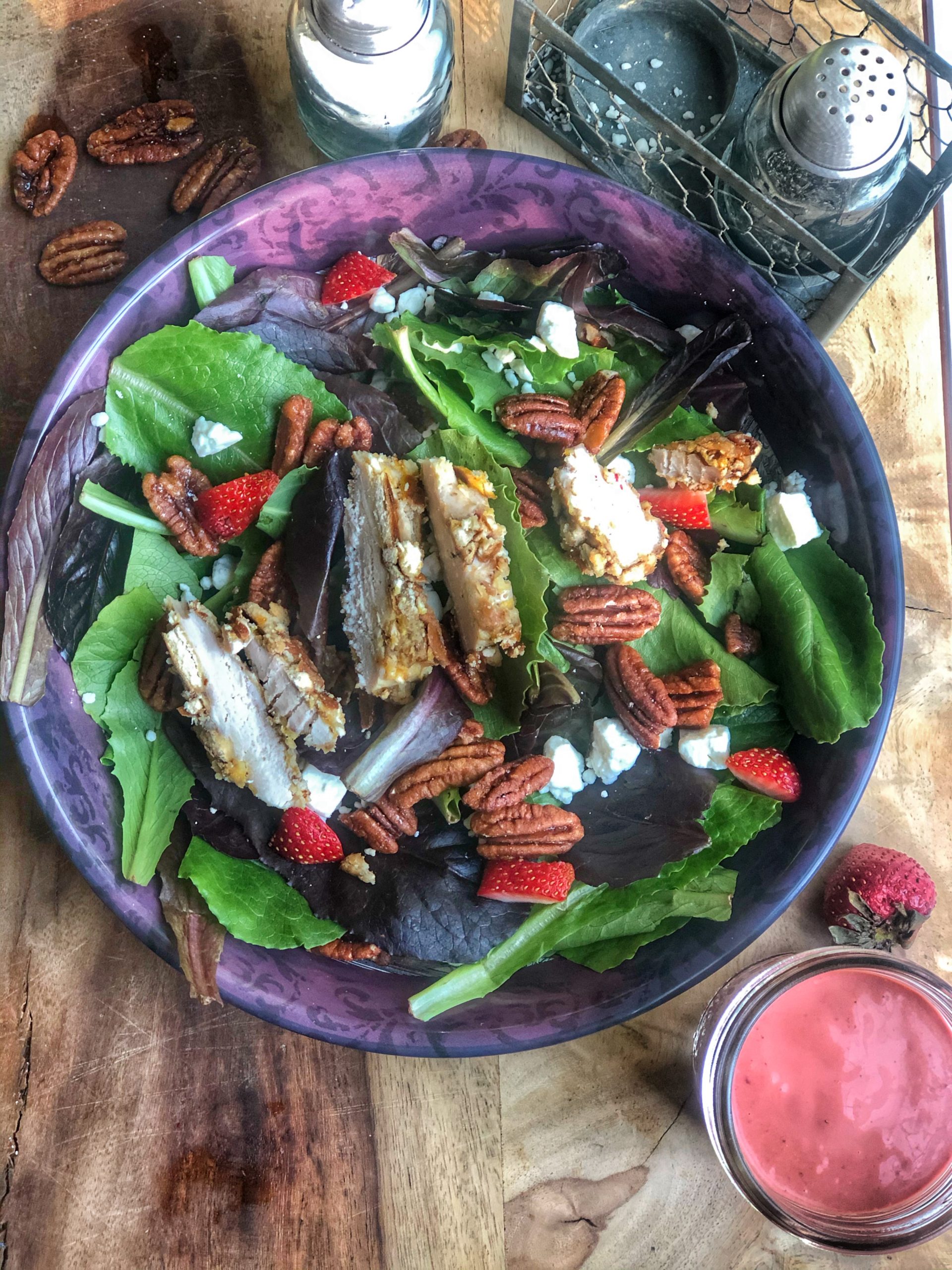 homemade strawberry vinaigrette dressing pictured with a salad on a wooden board