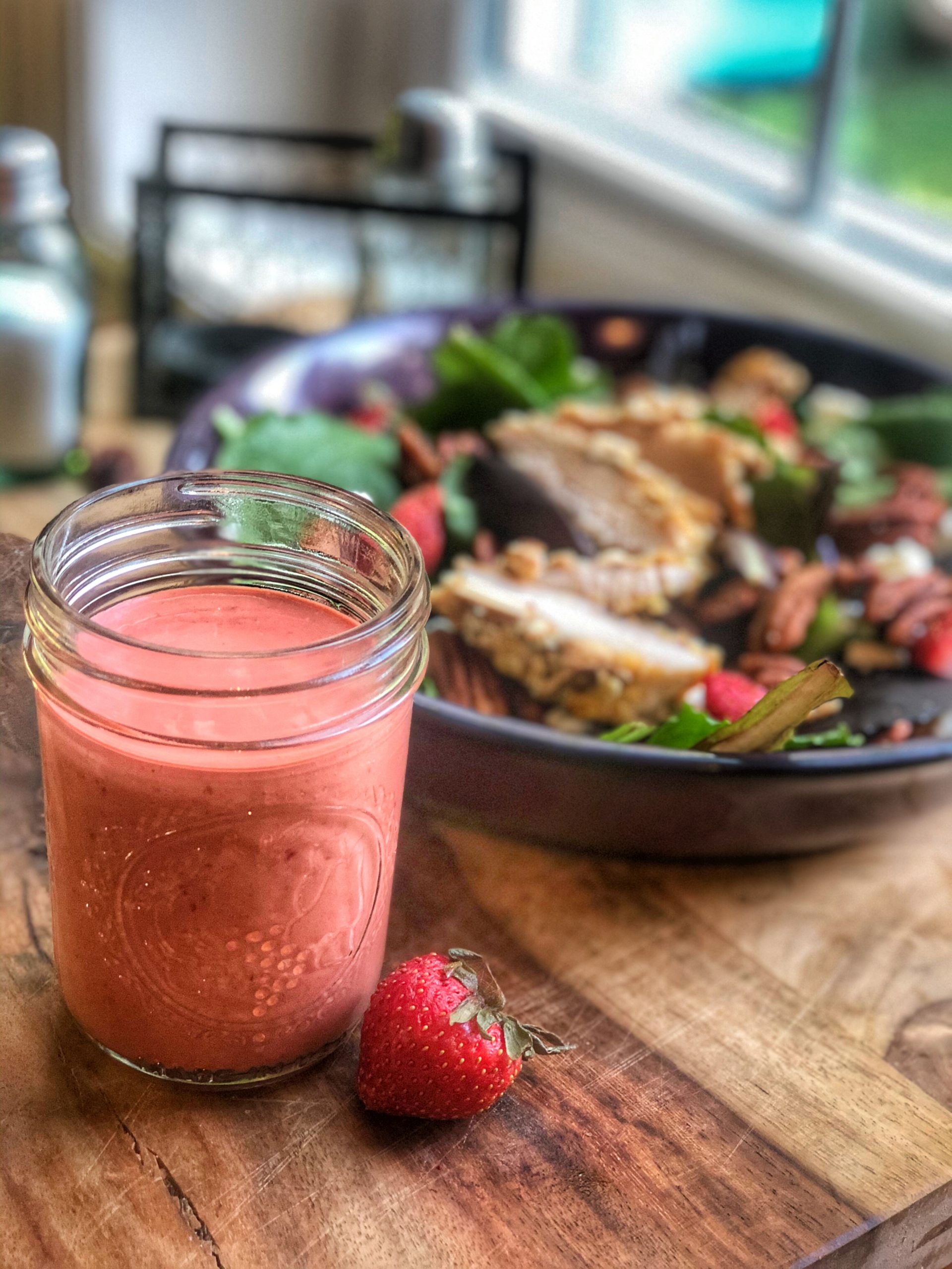 homemade strawberry vinaigrette dressing in a glass container with a salad in the background