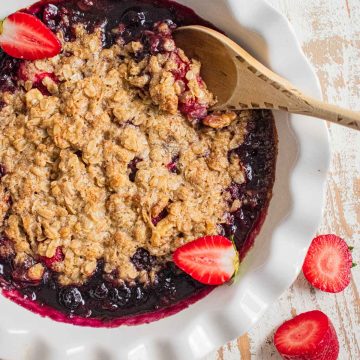 birds-eye view of a gluten-free fruit crisp in a white pie dish with fresh sliced strawberries on top