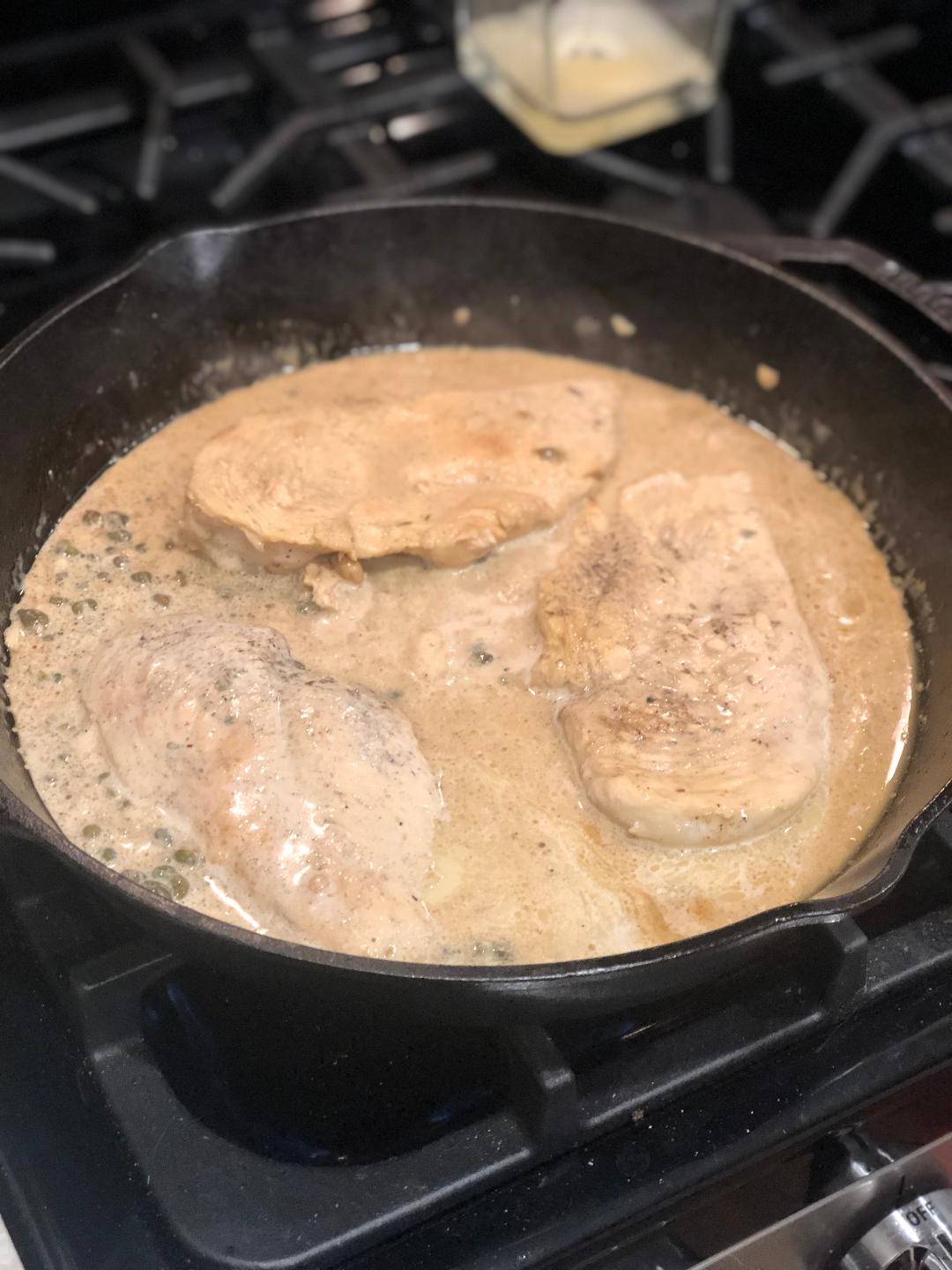 lemon garlic chicken cooking away in a cast iron skillet on the stove