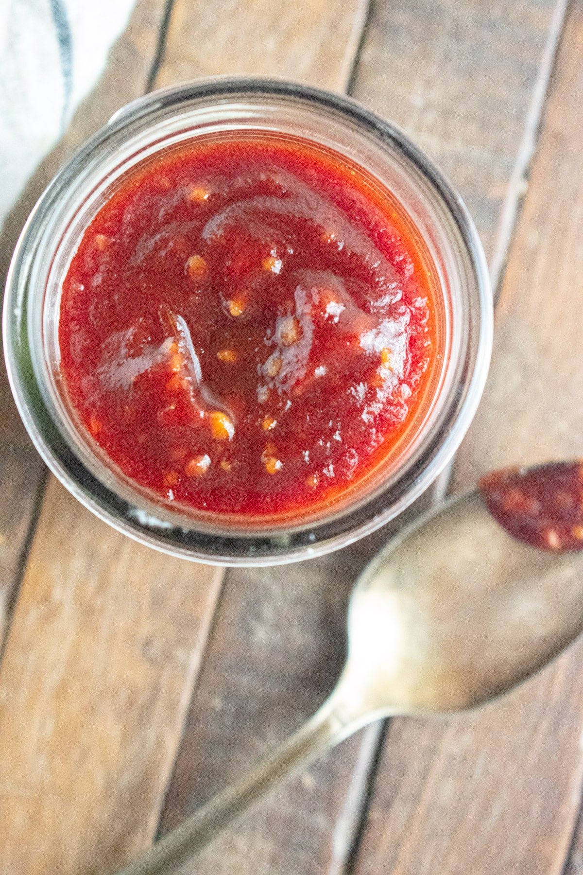Close up of homemade healthy BBQ sauce in a clear glass with a spoon laid next to it with a drop of BBQ sauce on it.