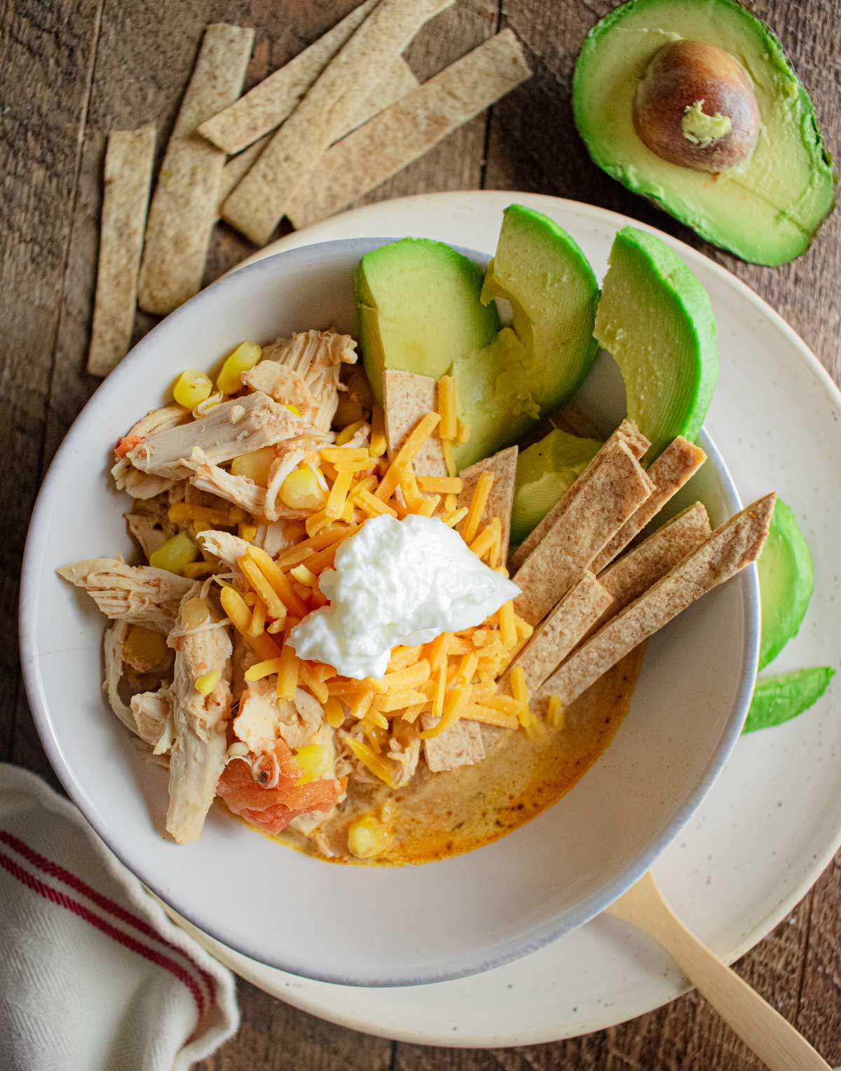 slow cooker healthy chicken tortilla soup in a white bowl with avocado and tortilla strips on top