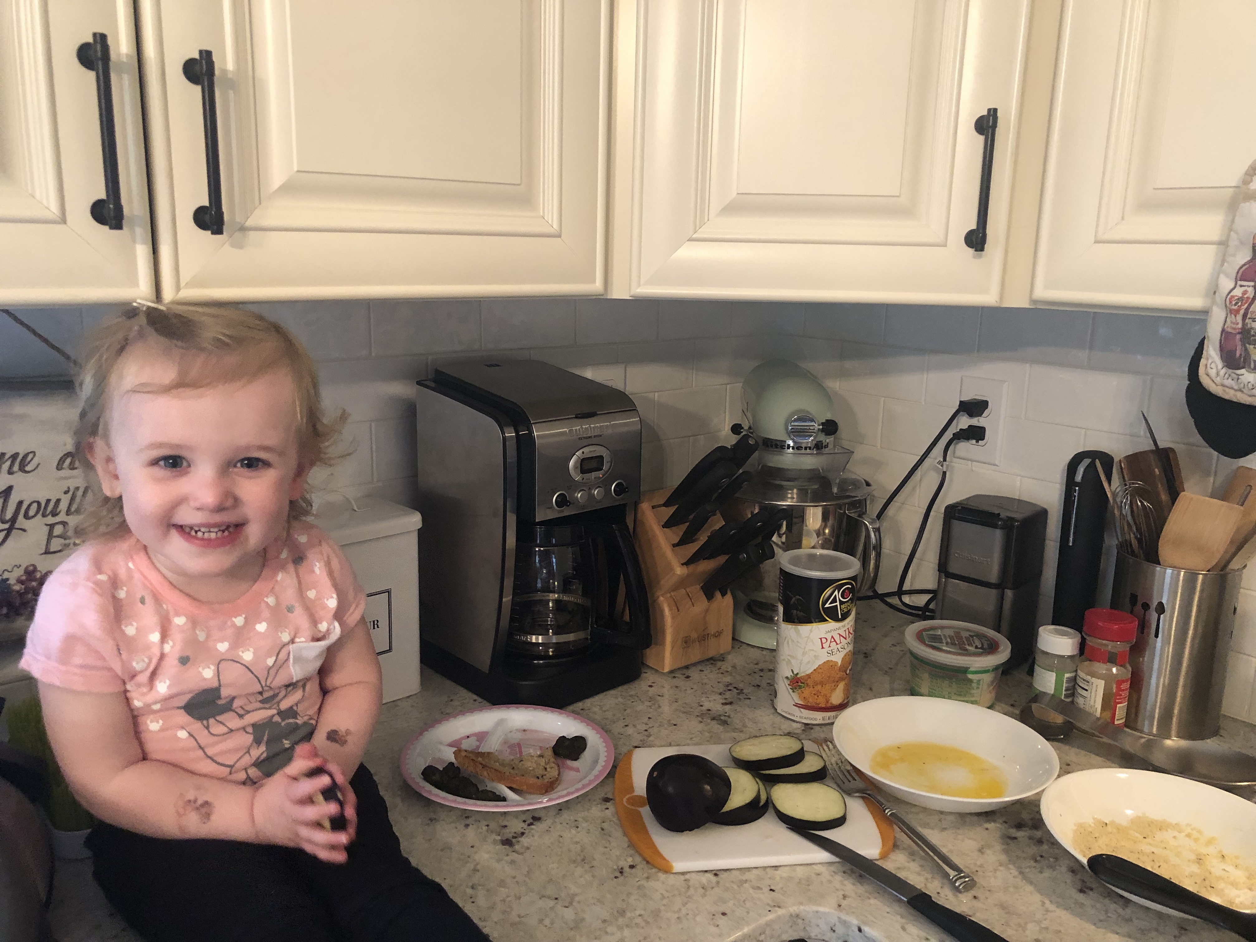 little blonde girl smiling with all the ingredients lined up on a counter