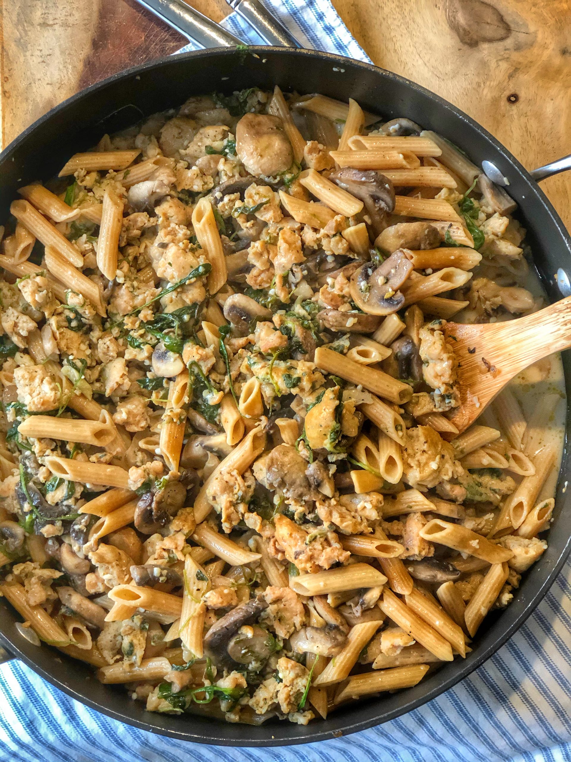 chicken sausage with a creamy mushroom penne sauce in a large frying pan with a wooden spoon