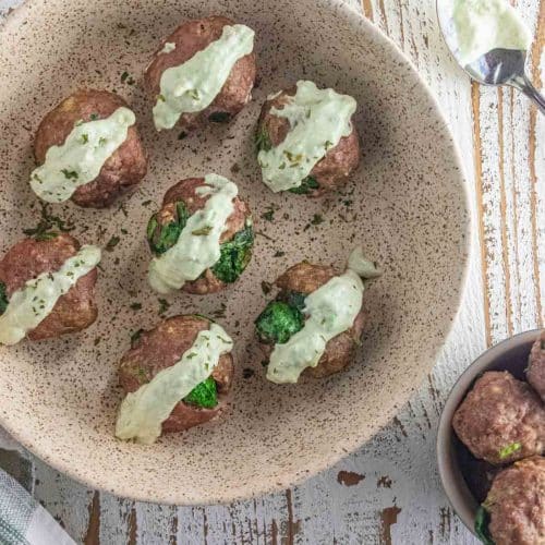 Air fryer turkey meatballs in a cream colored dish drizzled with creamy avocado dip in a cream colored bowl.